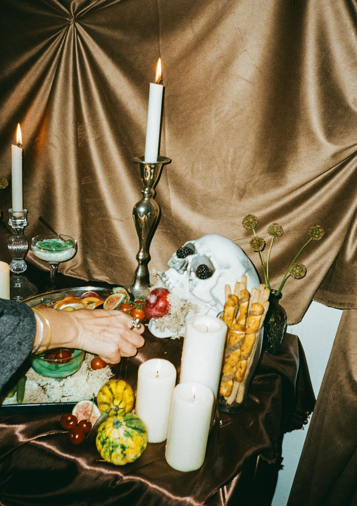 Halloween party spread with white candles, decorative gourds, and themed accessories on dark fabric.
