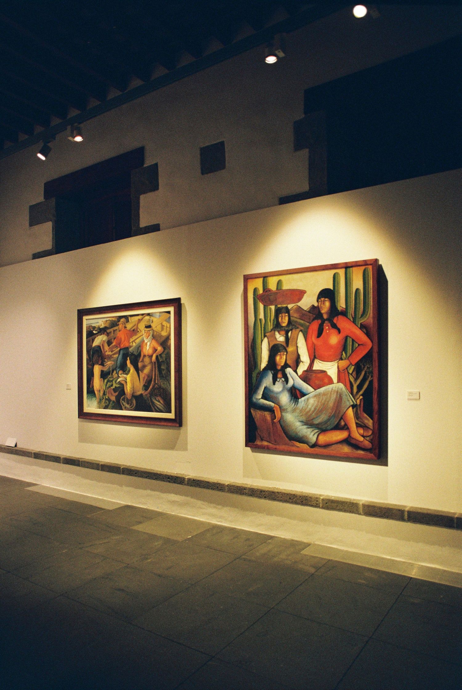 Art gallery wall displaying illuminated paintings in warm lighting.