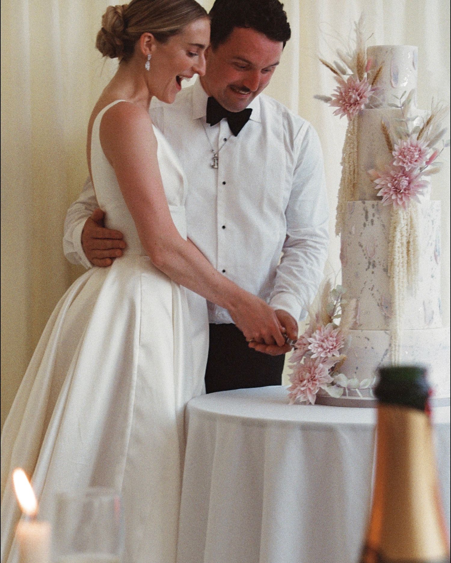 Wedding couple cutting cake together at reception with pink floral decorations.