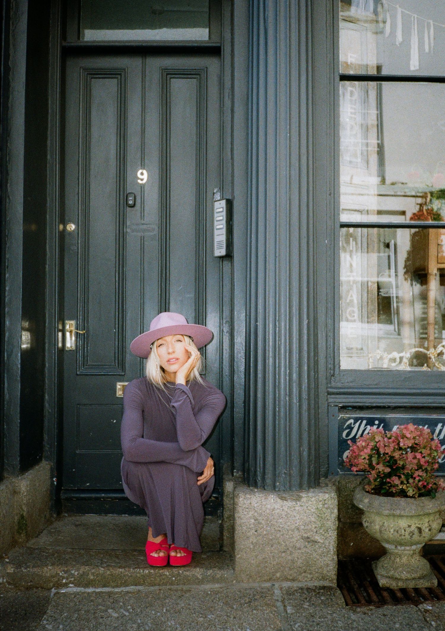 Whimsical fashion shots showing poses in purple dress and red shoes by a dark doorway.
