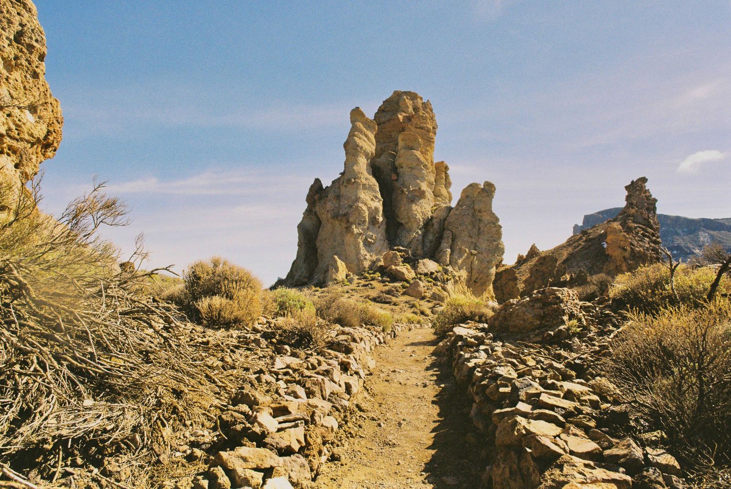 Rocky desert landscape with winding dirt path leading through rugged terrain under bright sunlight.