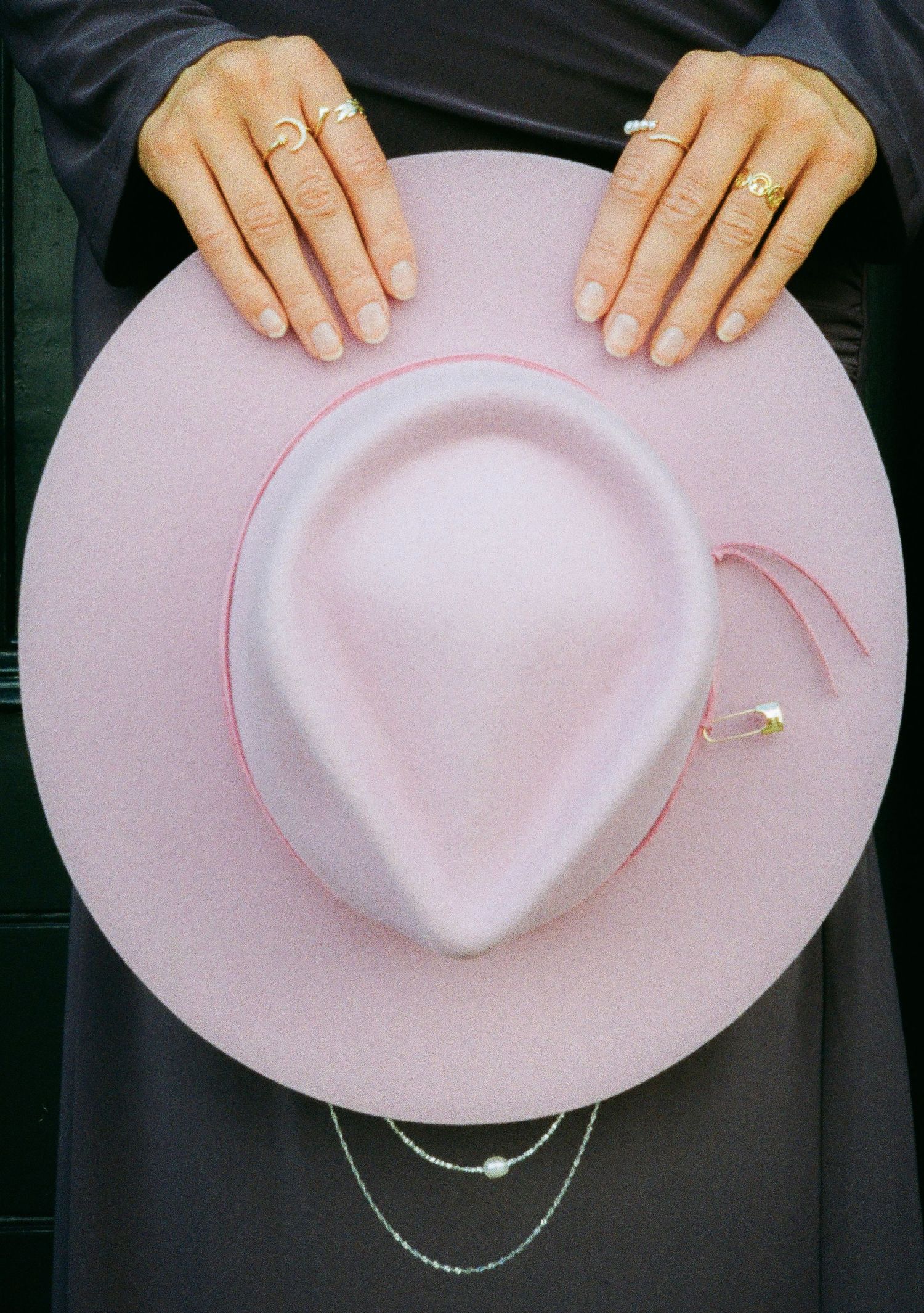 Close-up of hands holding a pink wide-brimmed hat against dark fabric.