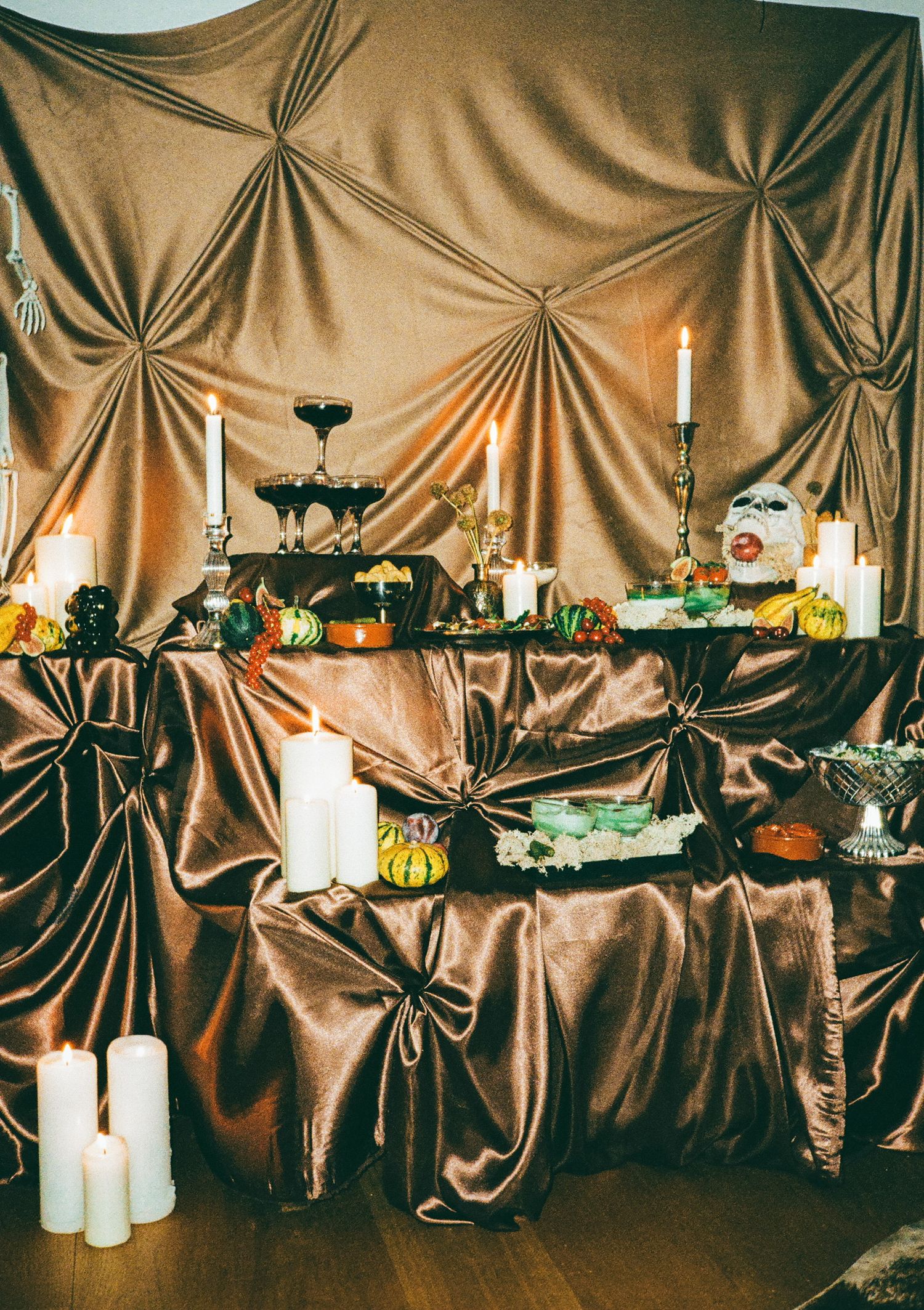 Decorative table display with candles and food items against draped brown fabric.