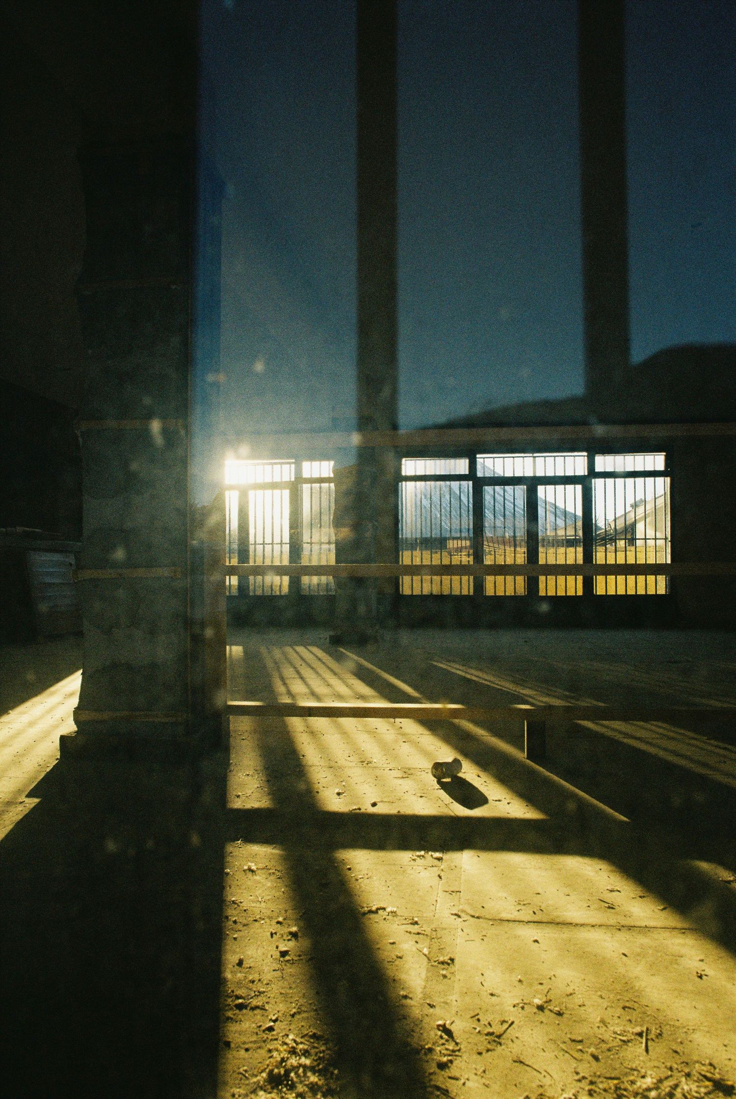 Sunlight streams through large windows casting dramatic shadows on an empty concrete floor.