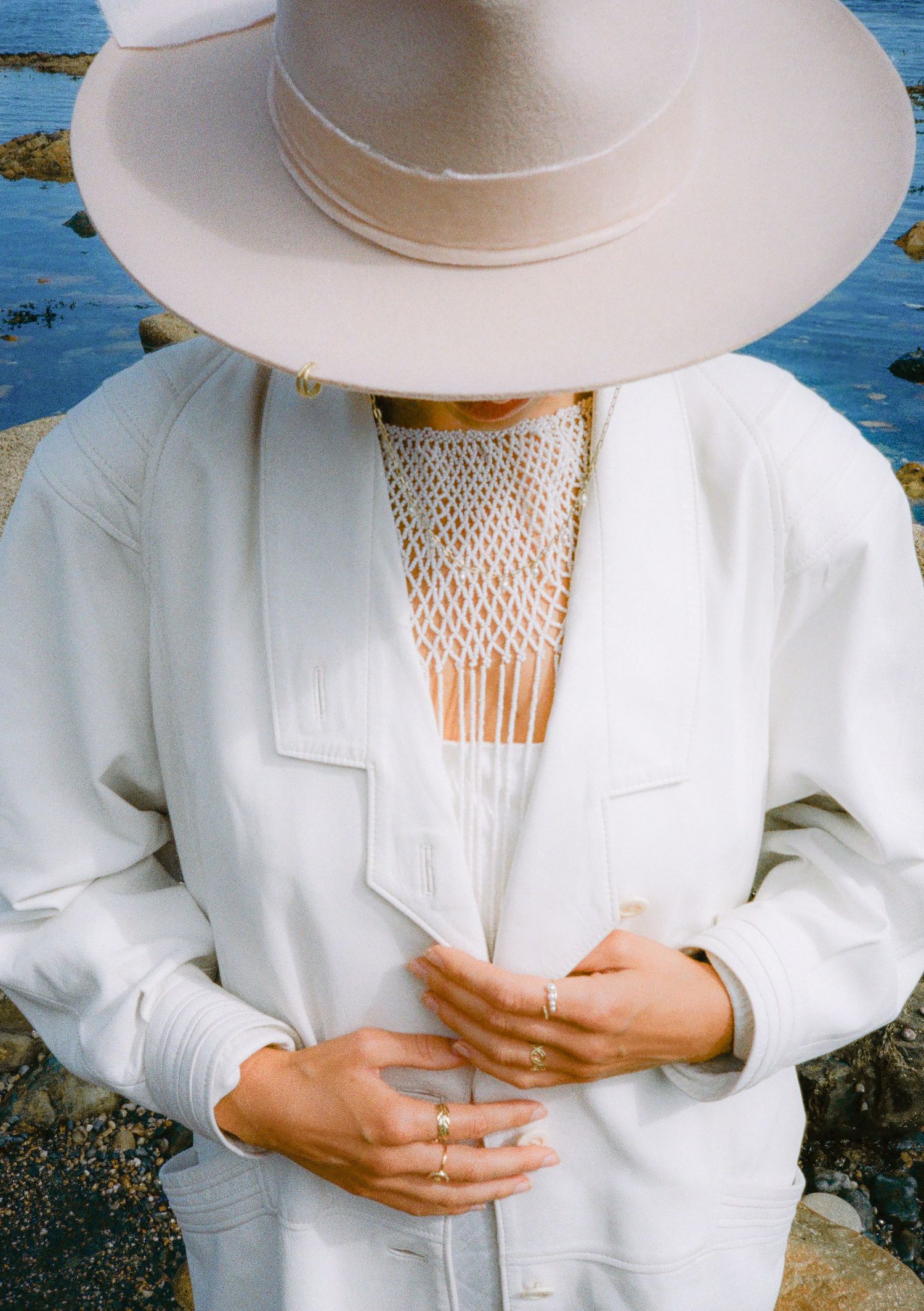 Close-up detail shots of white blazer and wide-brimmed hat with macrame necklace.
