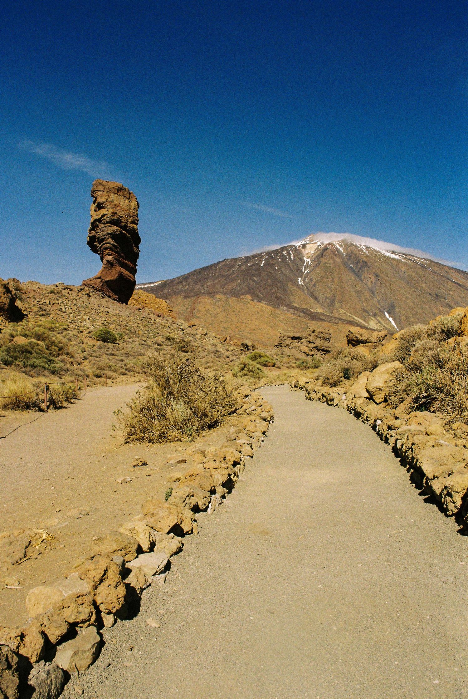 A winding path leads to a unique rock formation with Mount Teide volcano visible in the background under blue skies.
