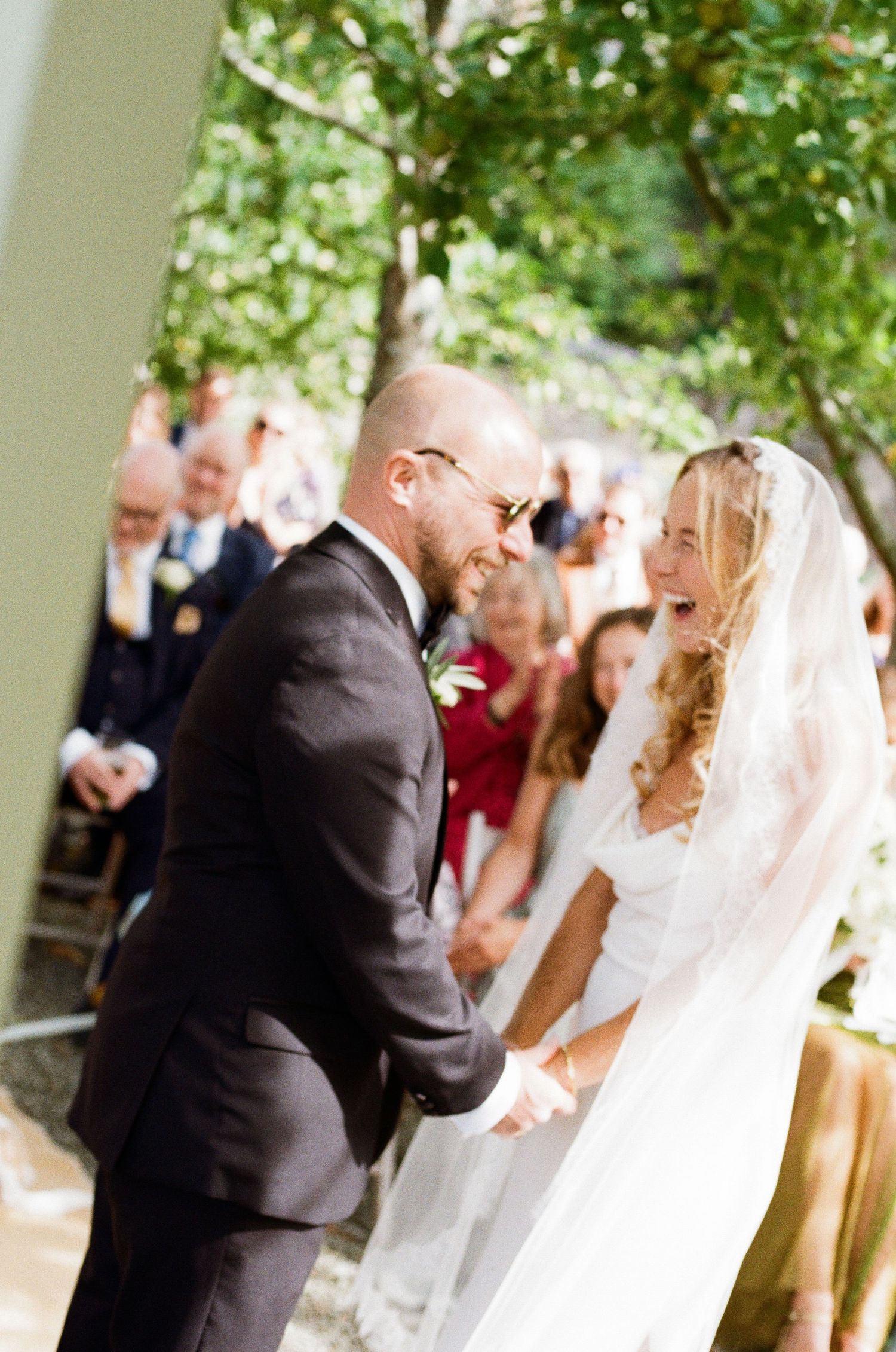 A joyous wedding ceremony moment under green foliage with guests watching.