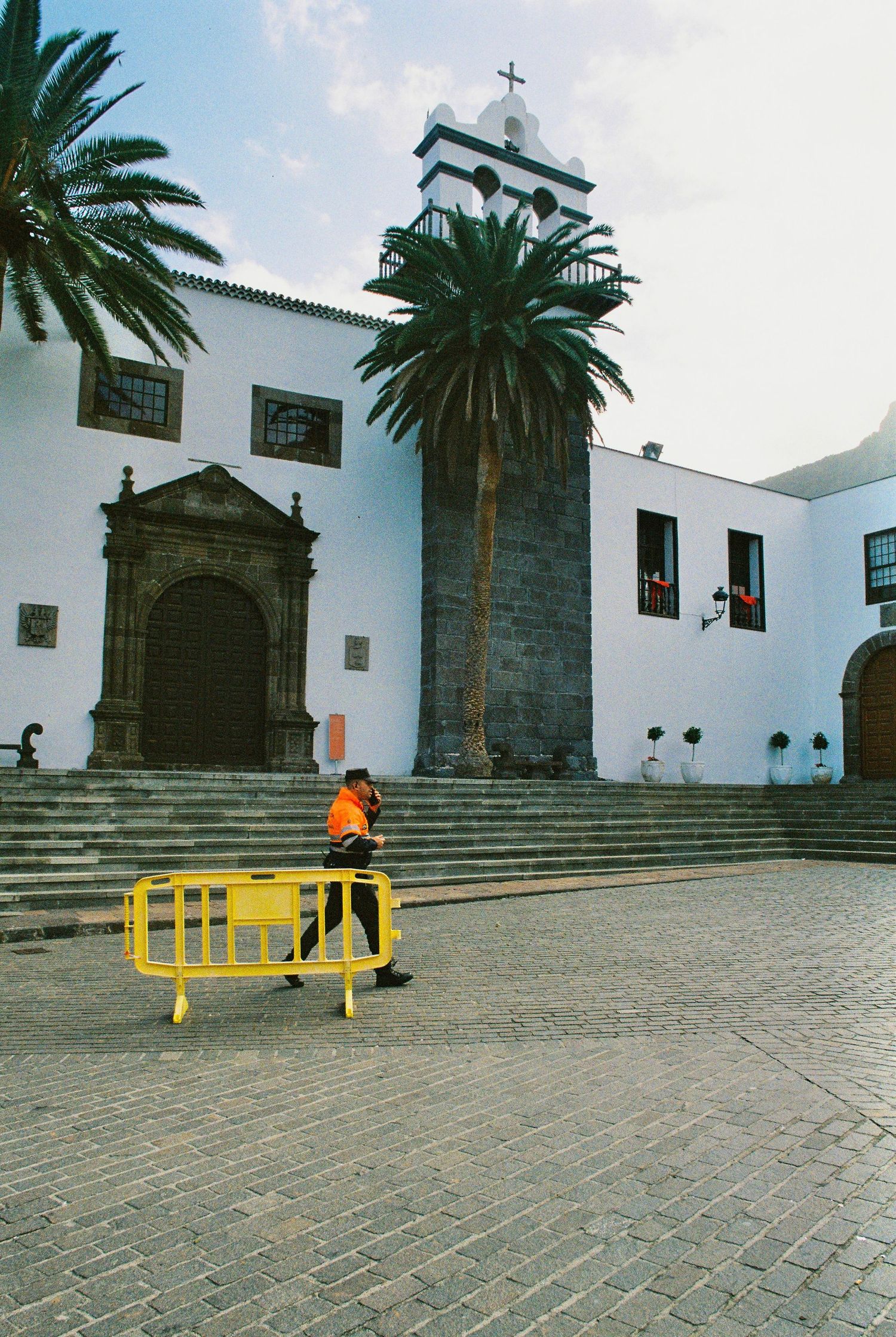 White Spanish colonial church with palm trees and a yellow barrier on stone steps in the foreground.