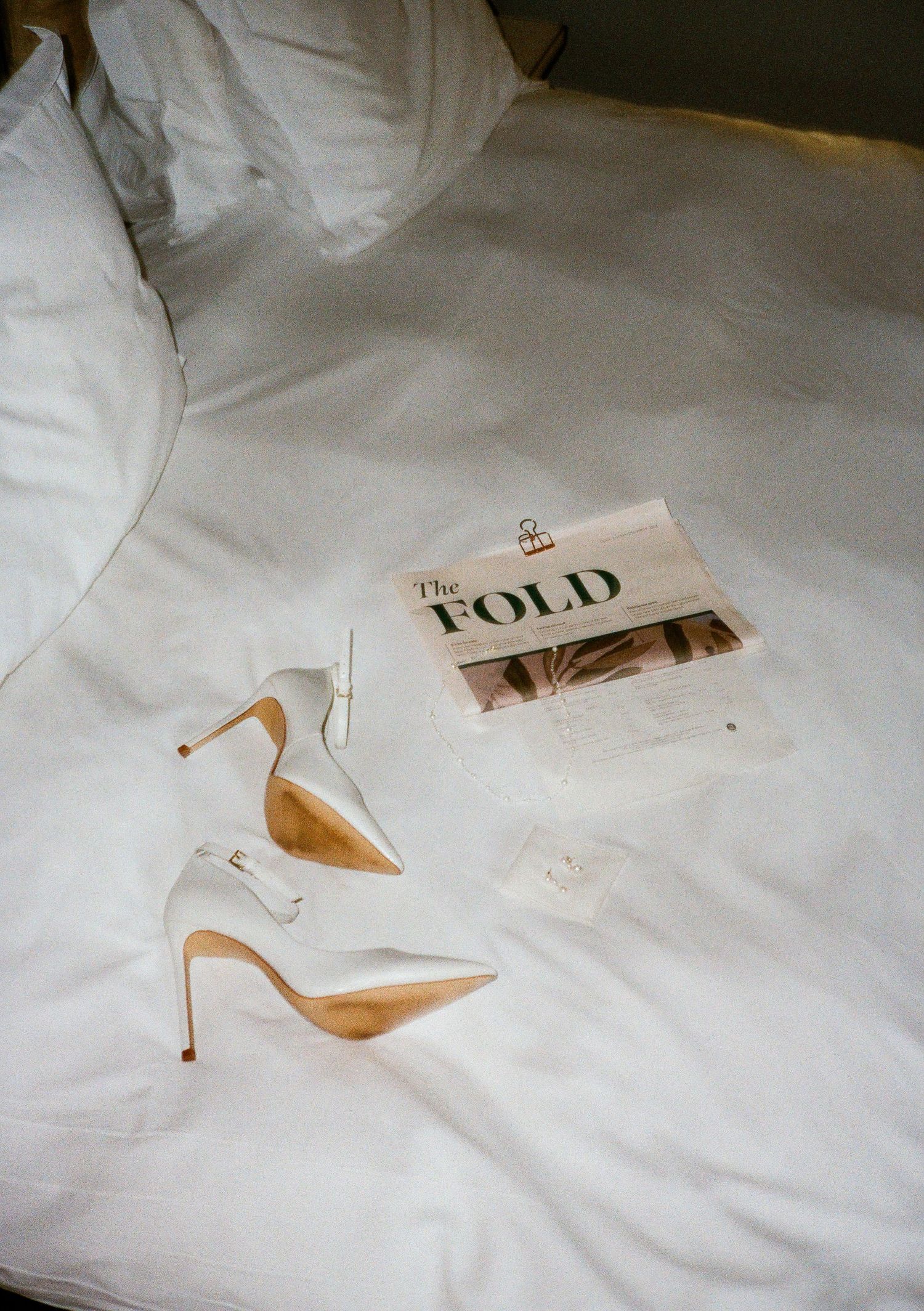 White high heel shoes and printed text scattered across white bedding.