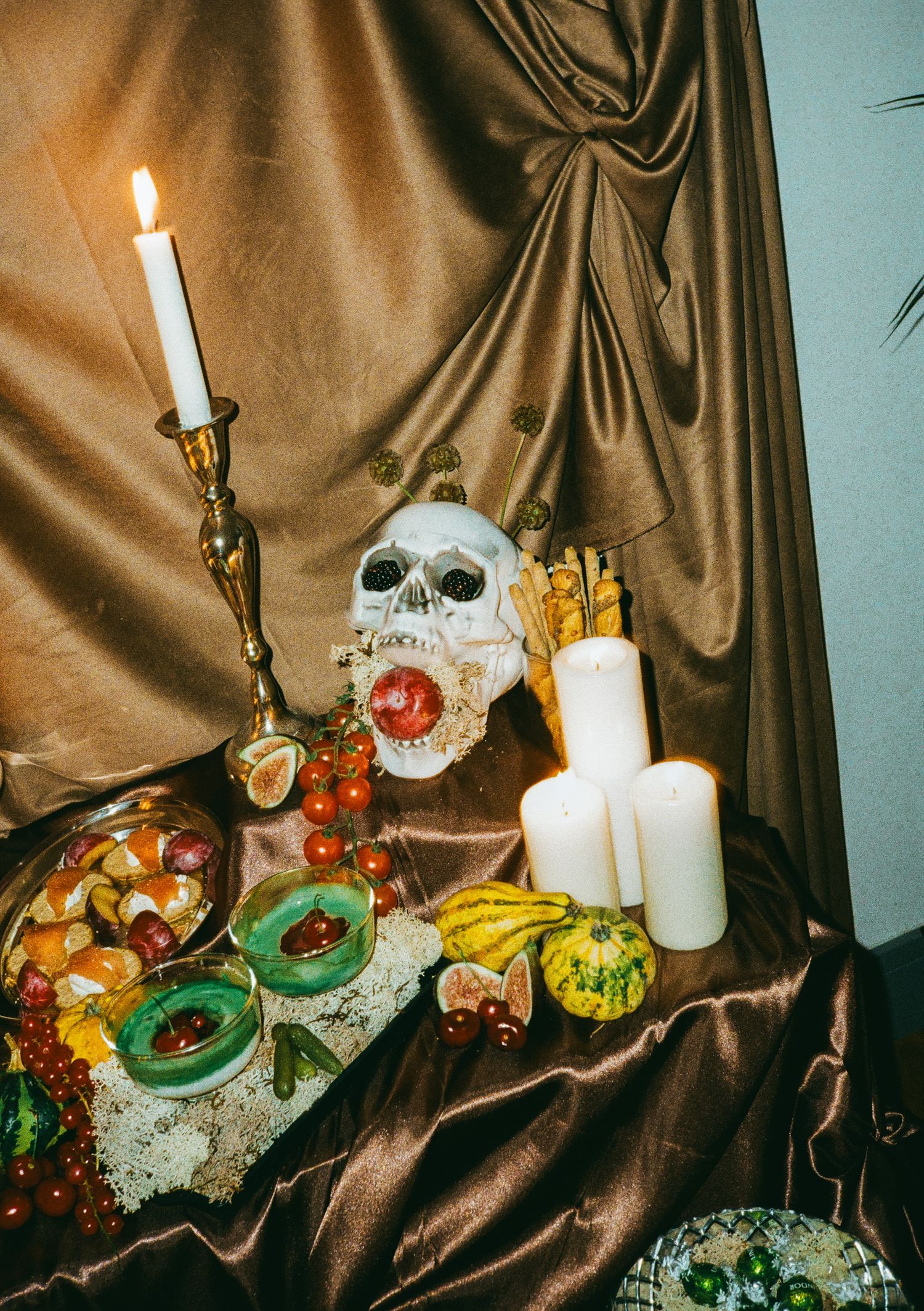 Elegant table setting with candles and food displayed on brown satin fabric backdrop.