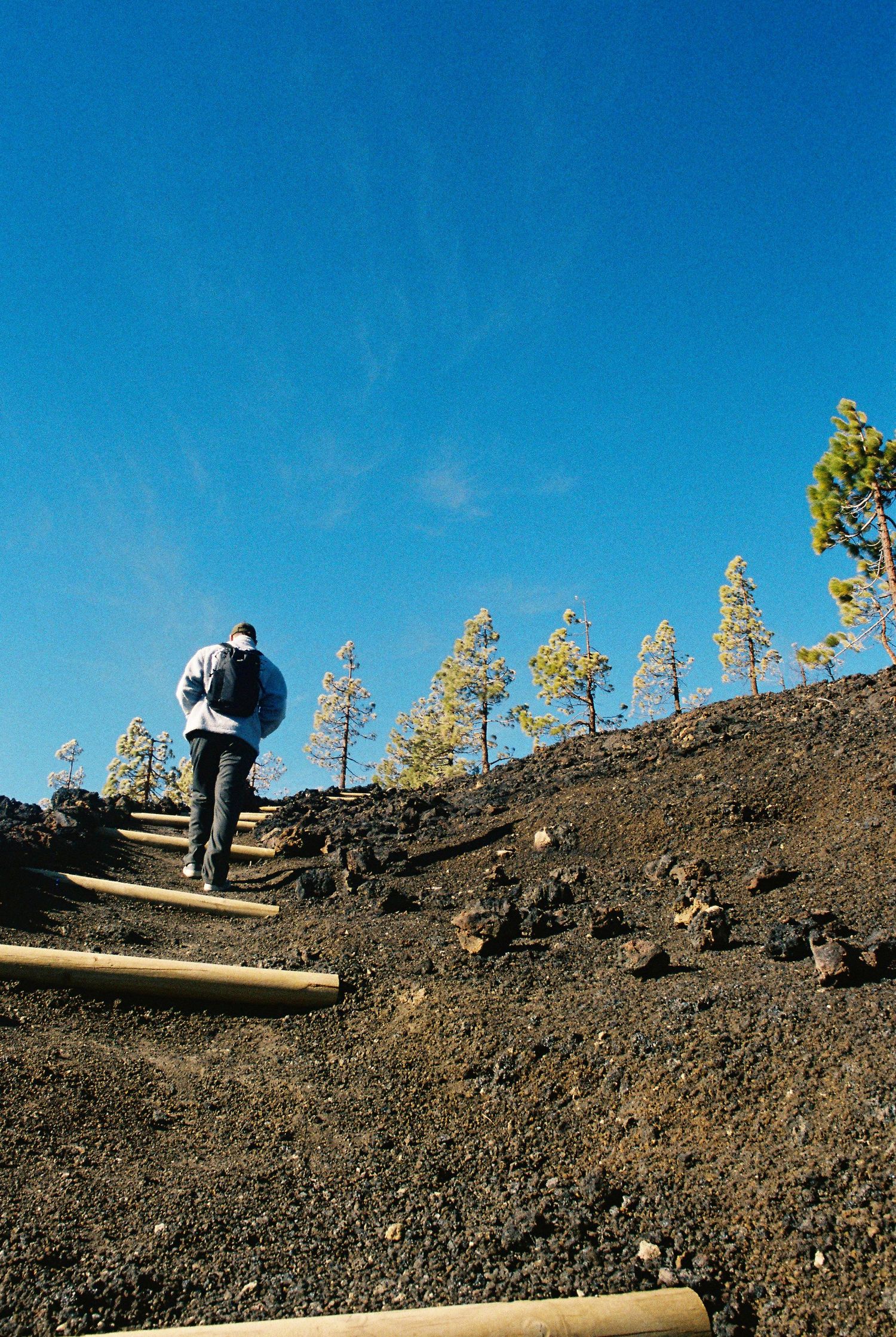Hikers traversing a rocky volcanic landscape against bright blue sky.