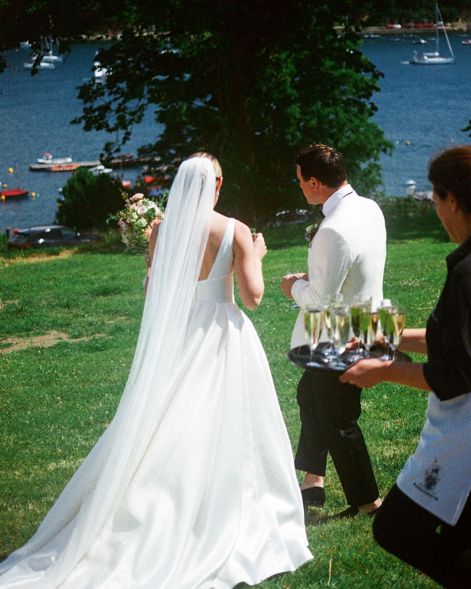 Wedding party taking photos outdoors near a waterfront with boats in the background.