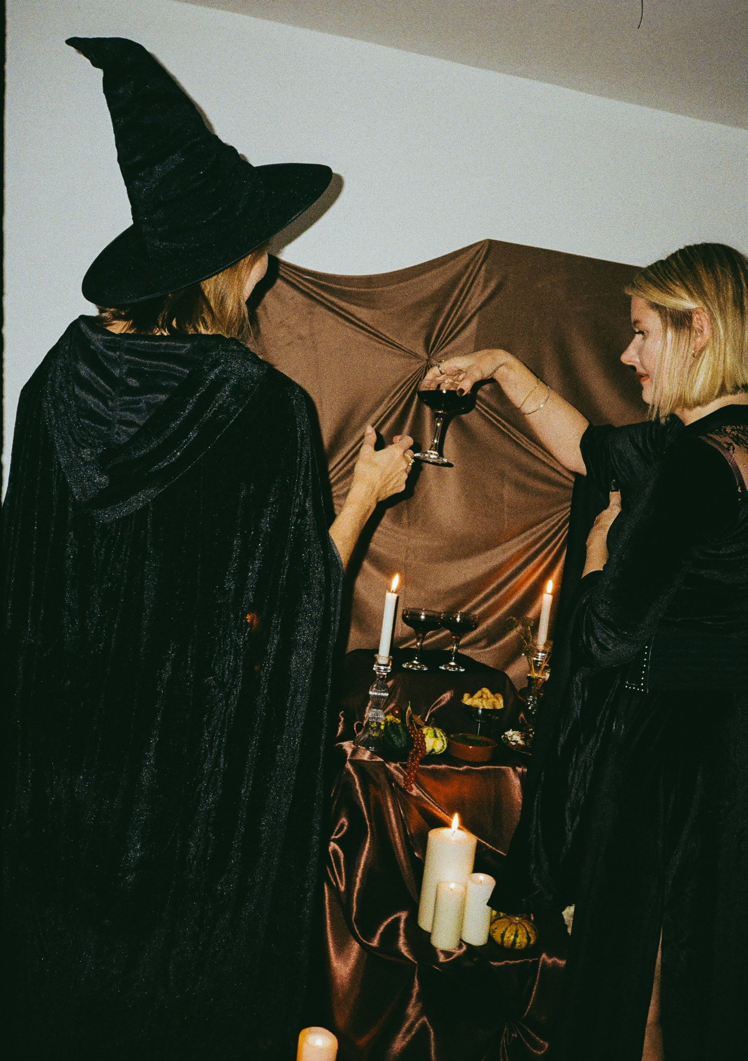 Dark silhouettes of figures in black cloaks against a brown backdrop at a Halloween gathering.