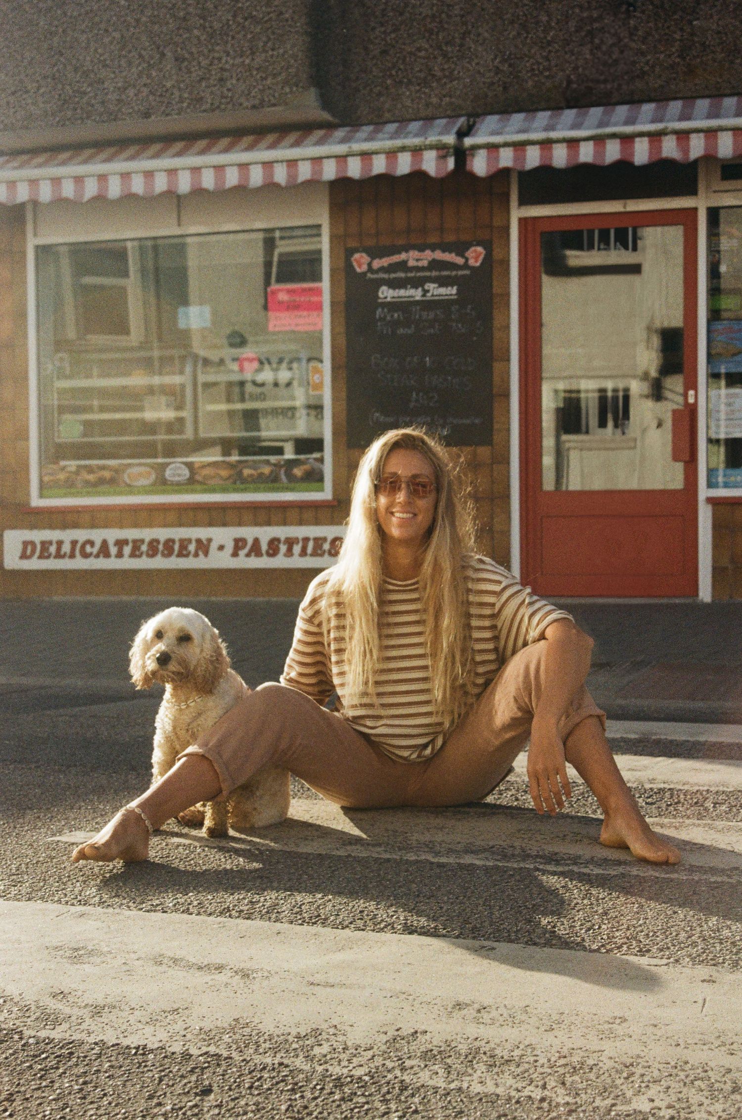 A person in a striped shirt lies on the ground with a dog outside a storefront.