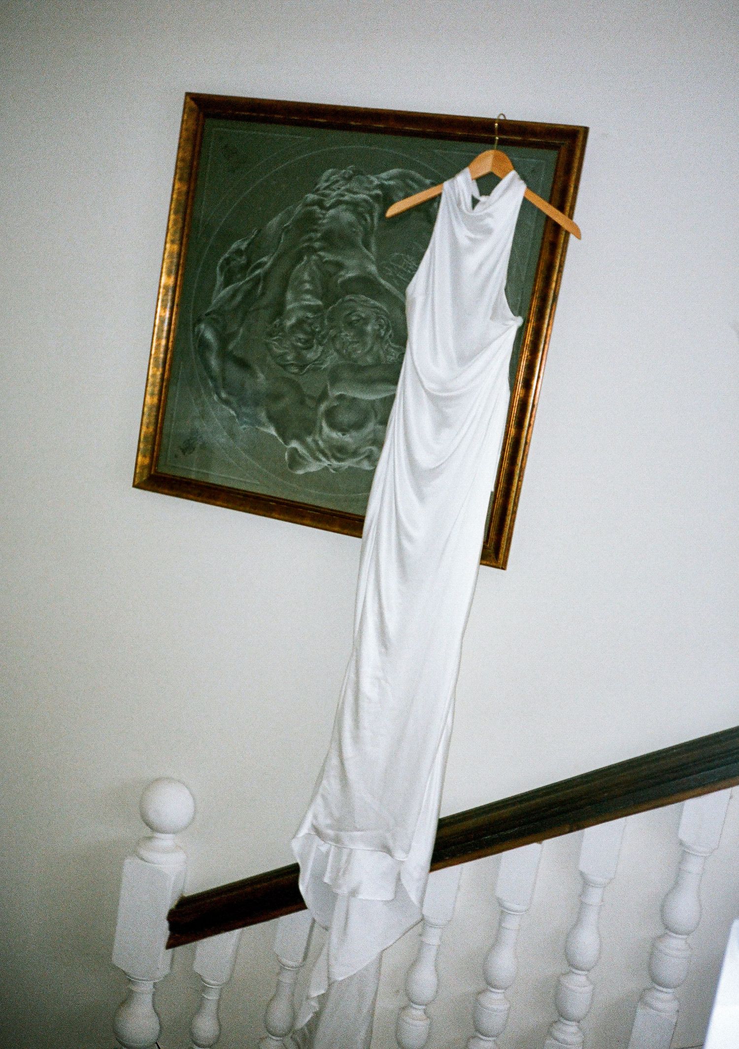 White wedding dress hanging against a wall with vintage picture frames.