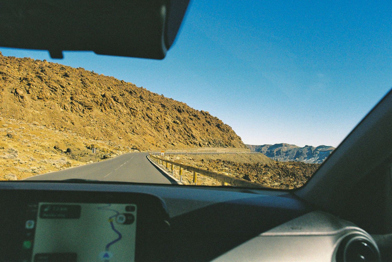 View through car windshield of winding desert highway with mountains in distance.