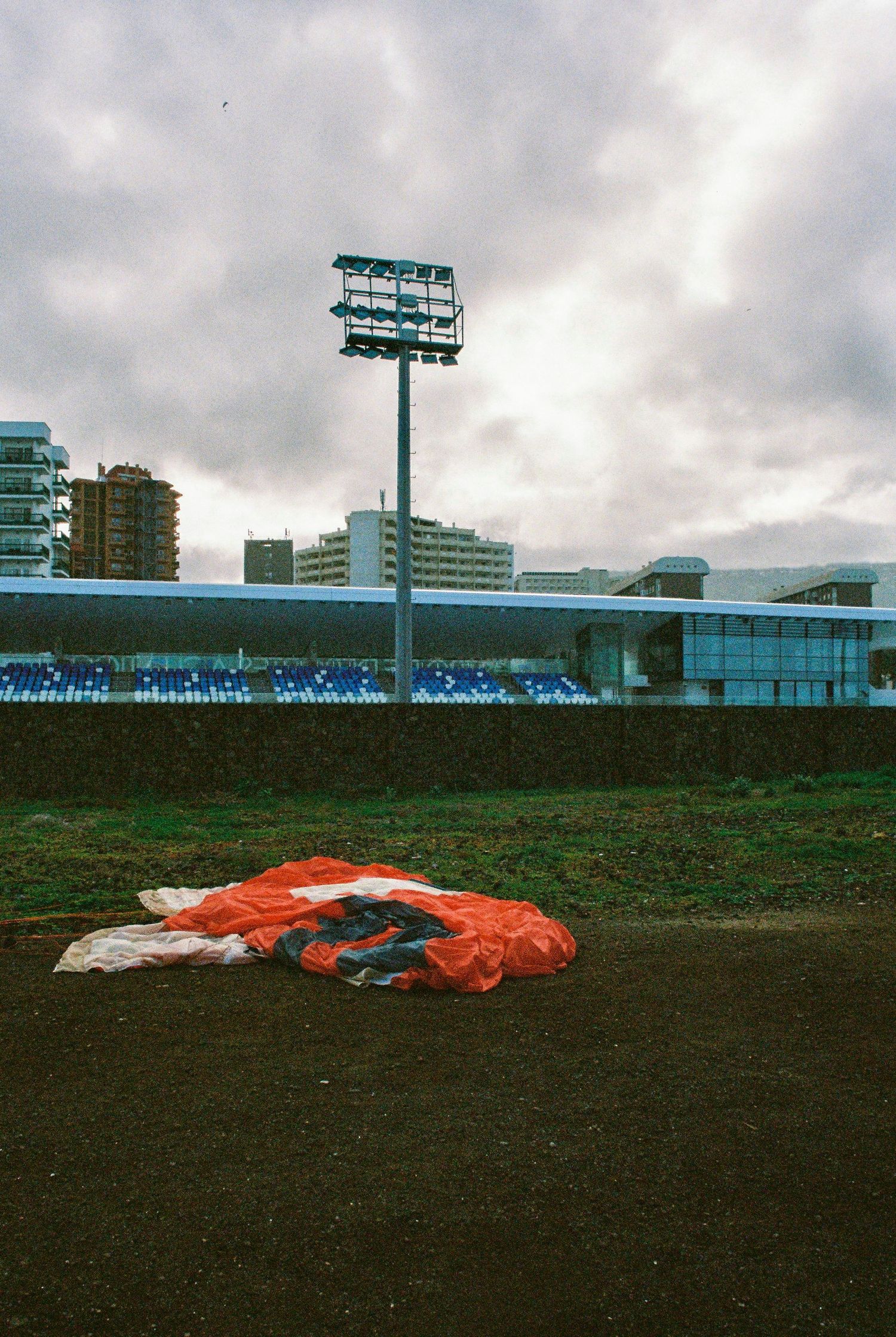 Red parachute lying on a grassy field with stadium lights and buildings in the background.