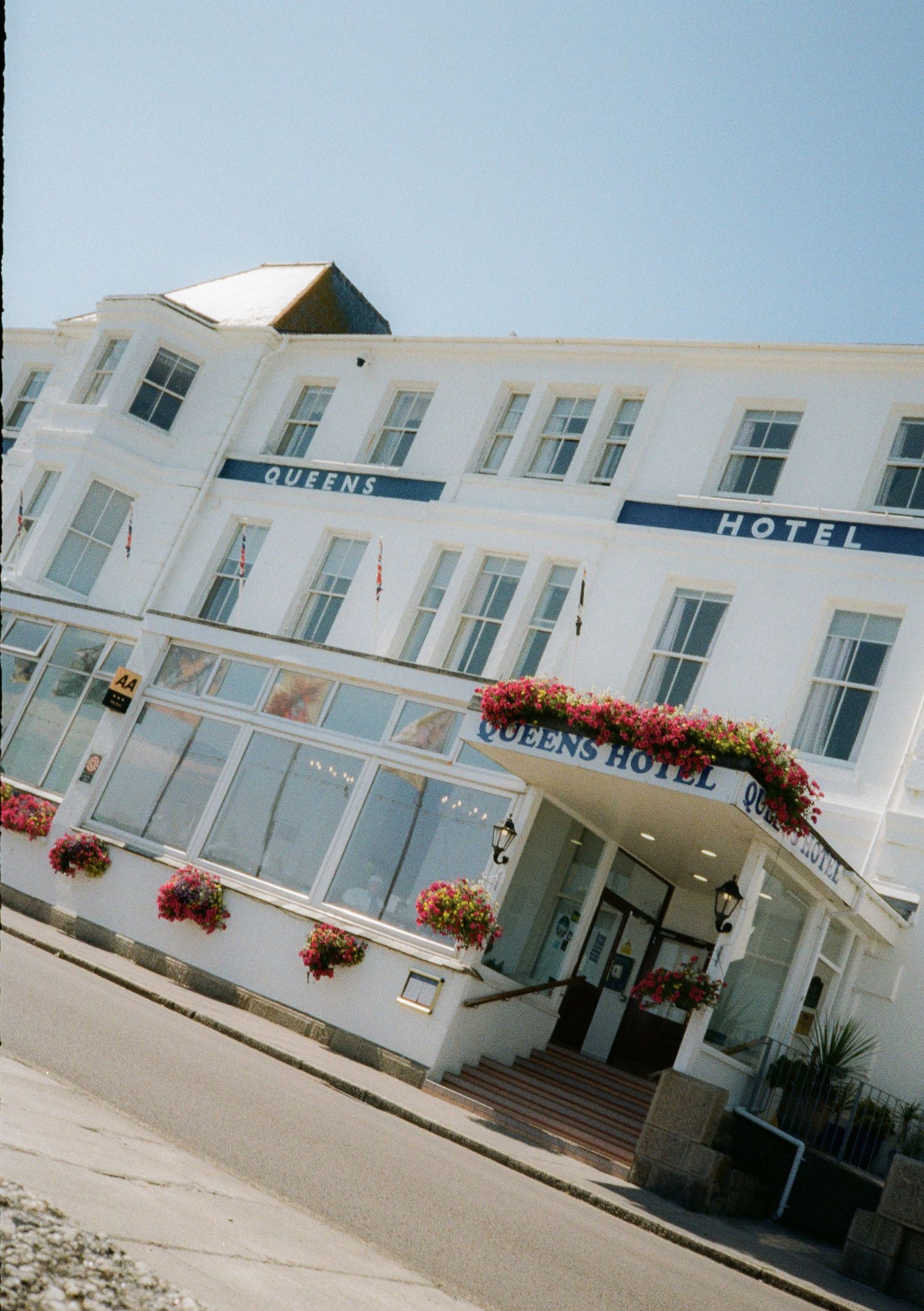 Exterior view of Queens Hotel with white facade and hanging flower baskets.