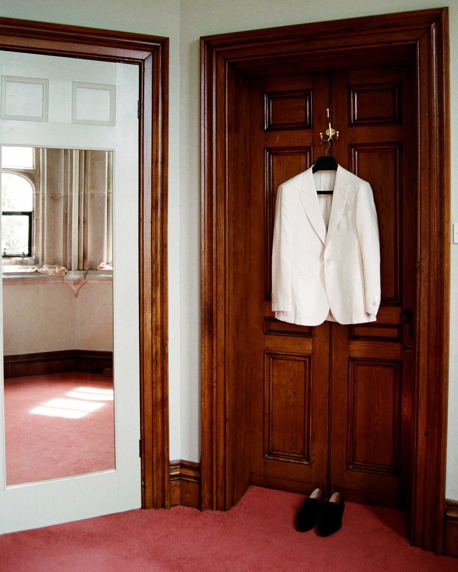 A sequence showing a white suit jacket and black pants hanging in a room with wooden doors and red carpeting.
