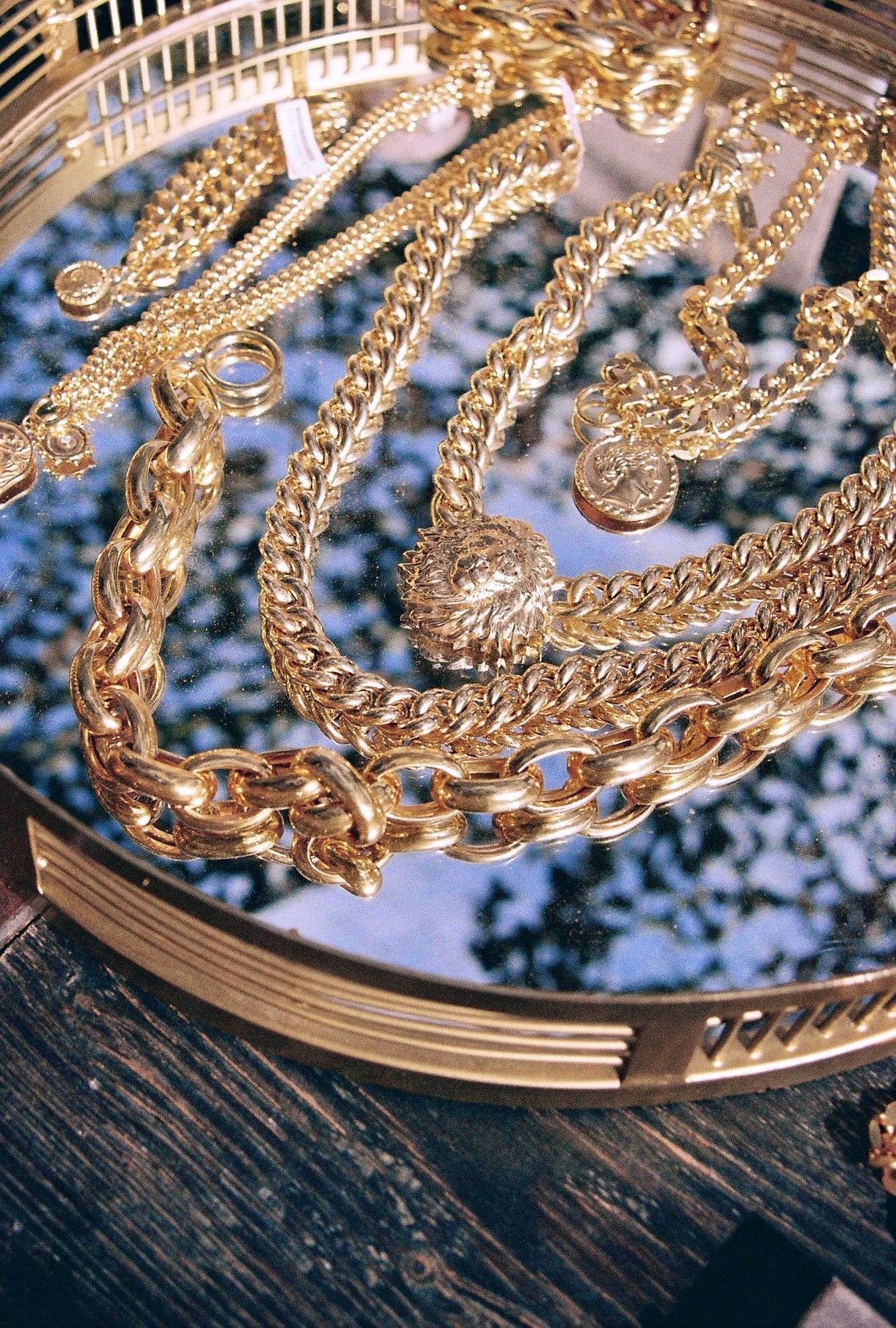 Gold chains and jewelry arranged on a dark wooden surface with reflective elements.