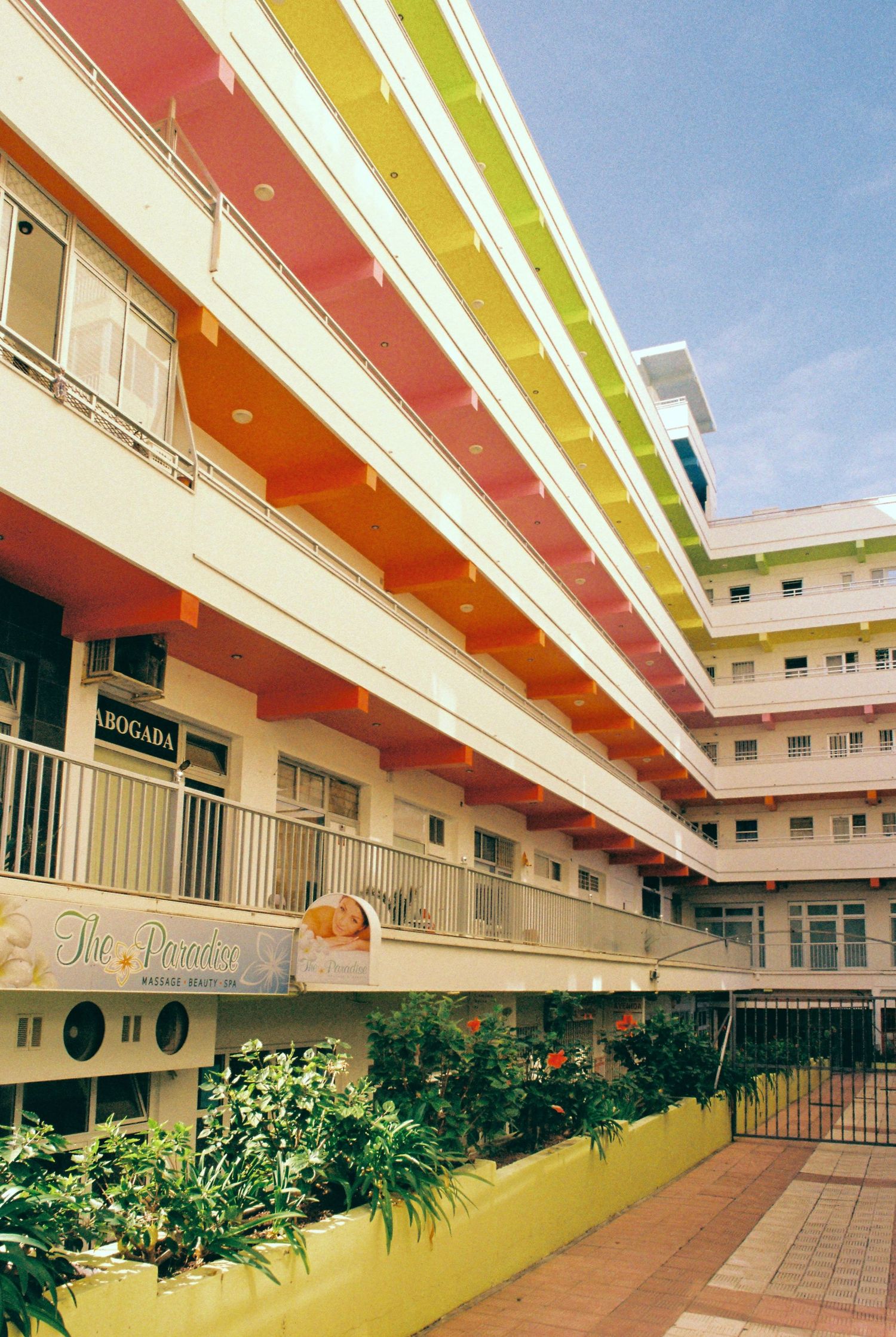 Colorful retro-style apartment building with yellow walls and red accents featuring a landscaped courtyard.