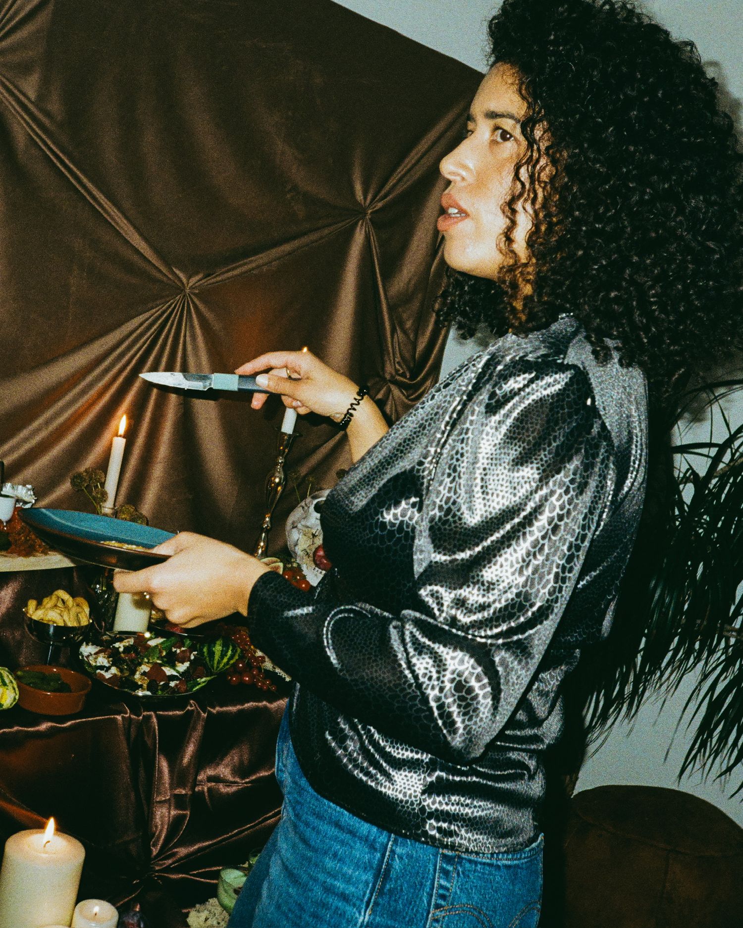 Person in sparkly silver top and jeans reaching for something at a party.
