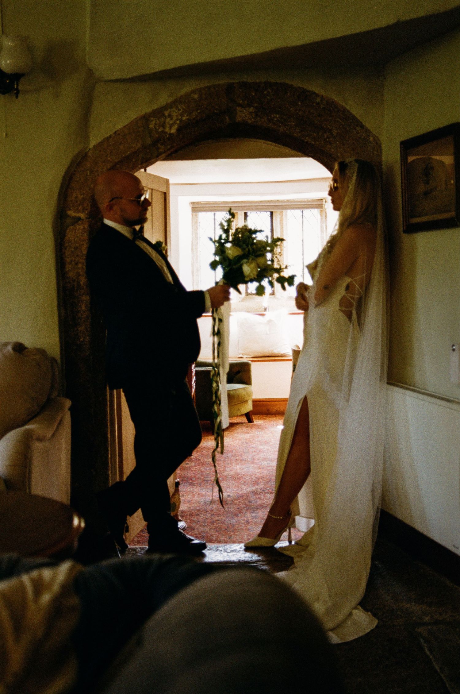 A wedding couple stands in a rustic stone archway during an intimate indoor ceremony.