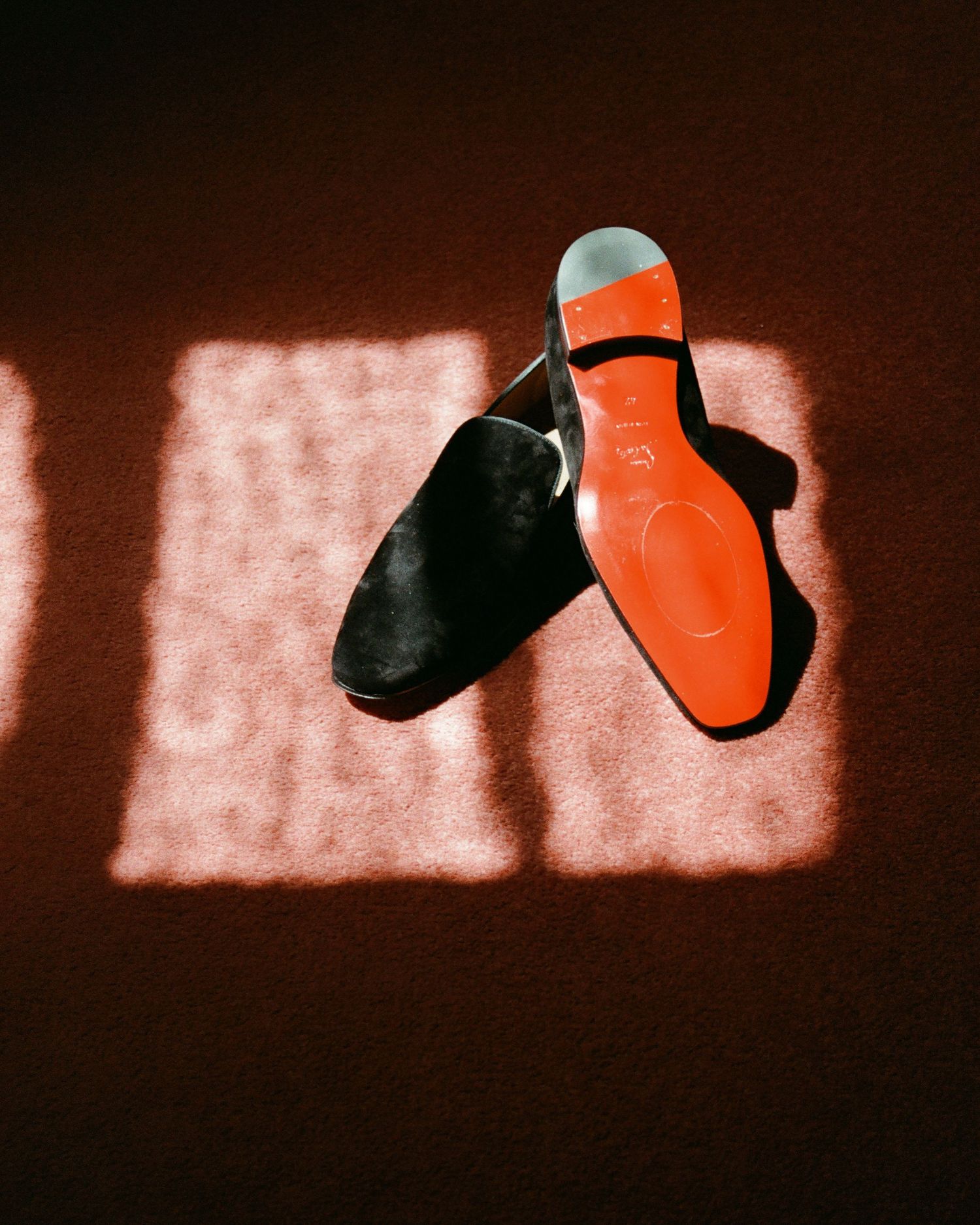 Artistic silhouette of orange and black shoes against a red-tinted wall.