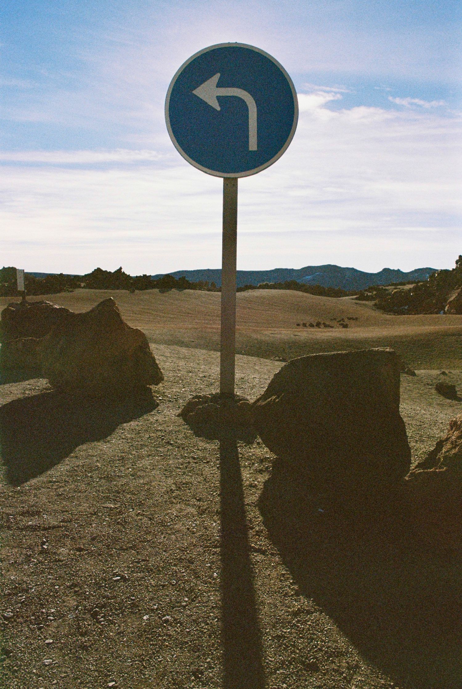 Directional road signs on desert path with rocky terrain and mountains.