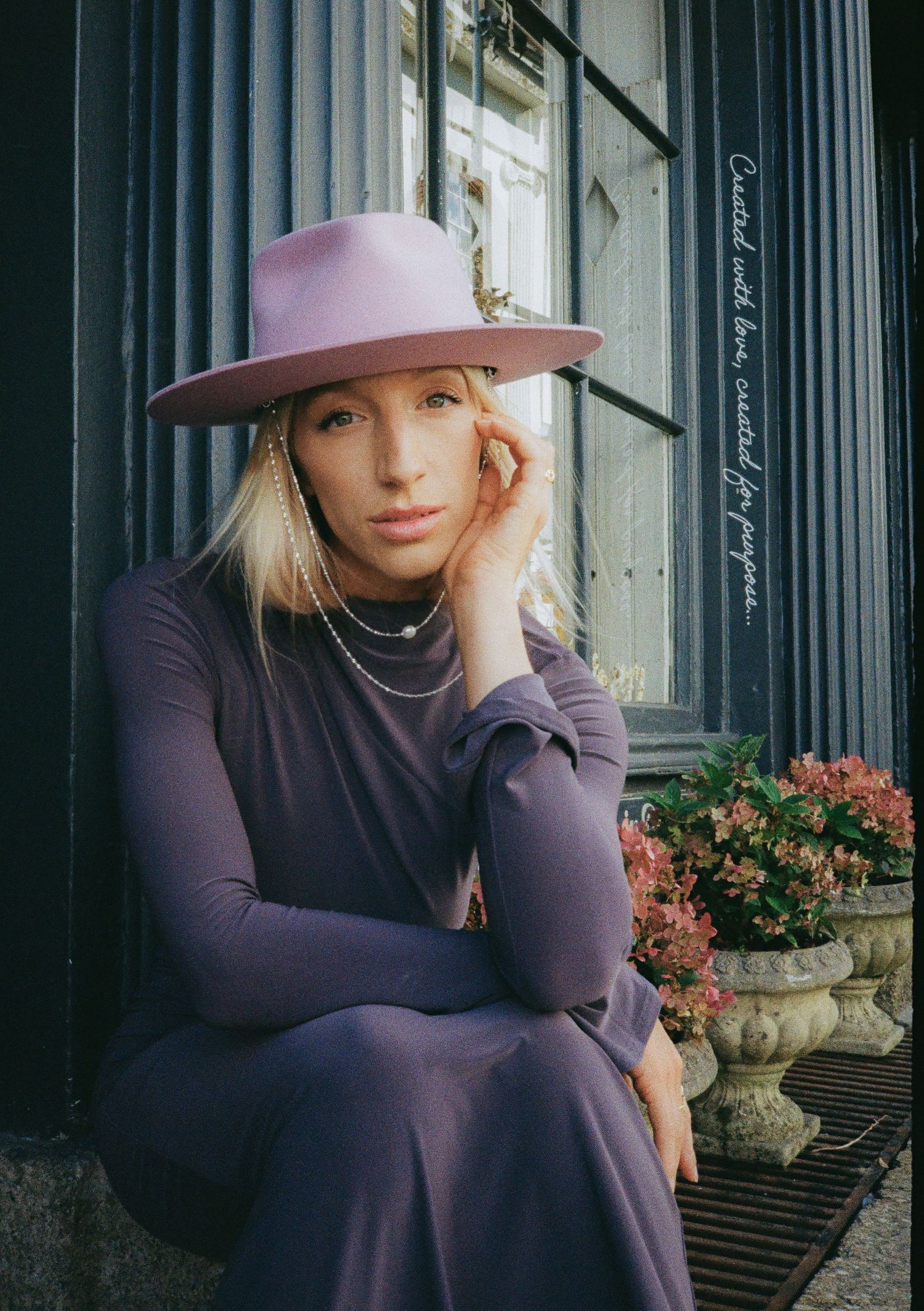 Moody fashion portrait with pink hat and purple dress against dark architectural columns.