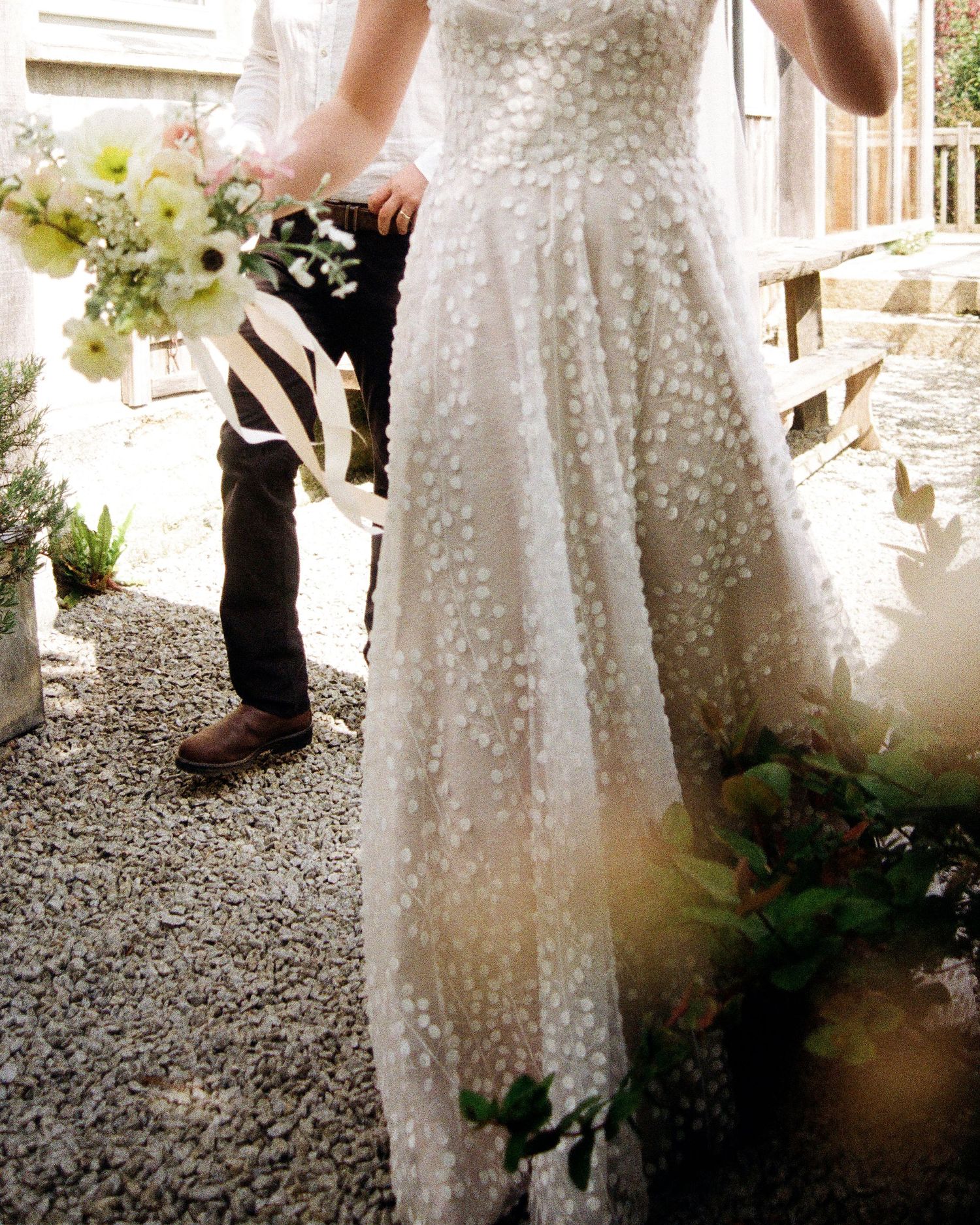 Close-up of textured white polka dot wedding dress against gravel path.