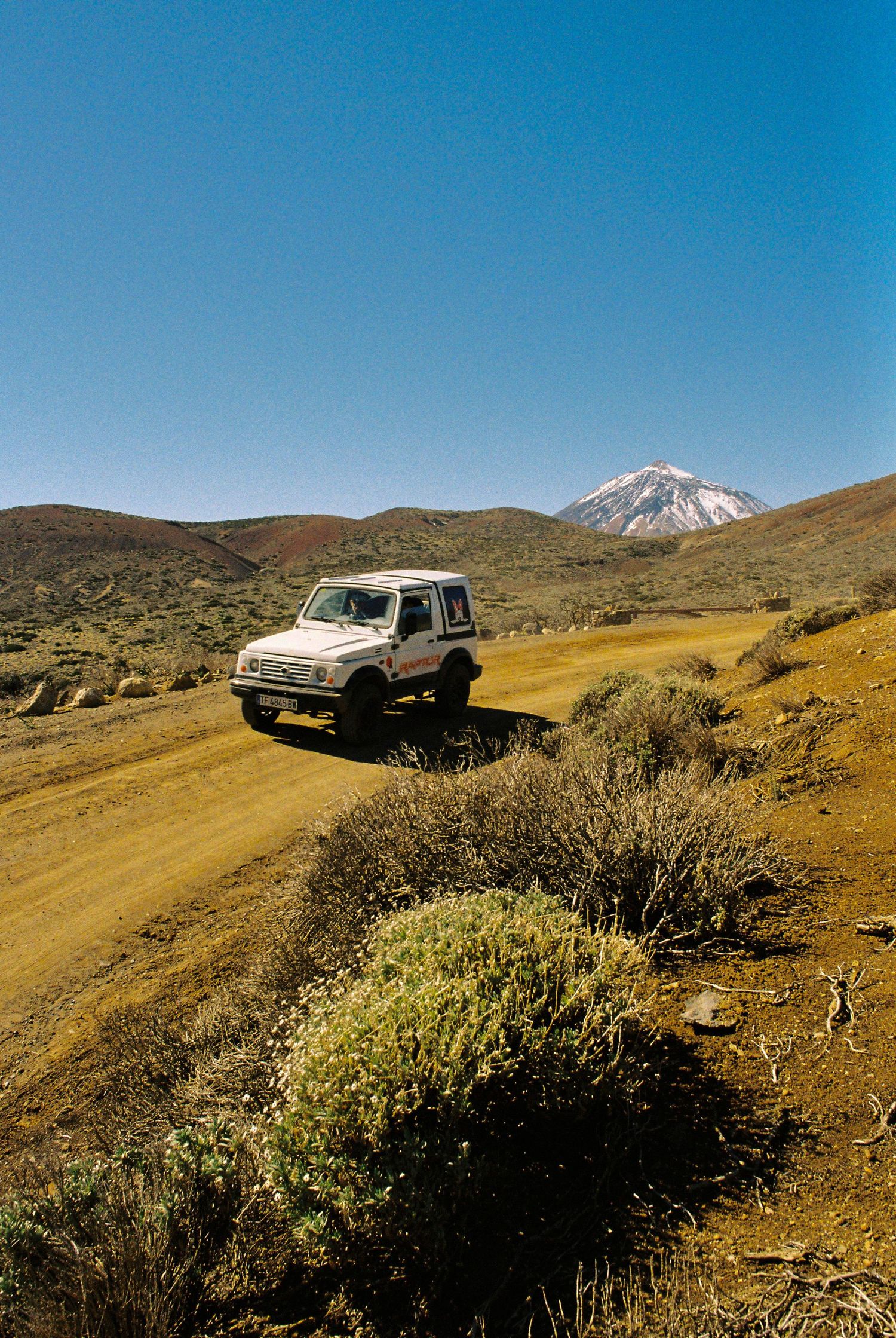 Classic car parked on a desert hillside with snow-capped mountains in the distance.