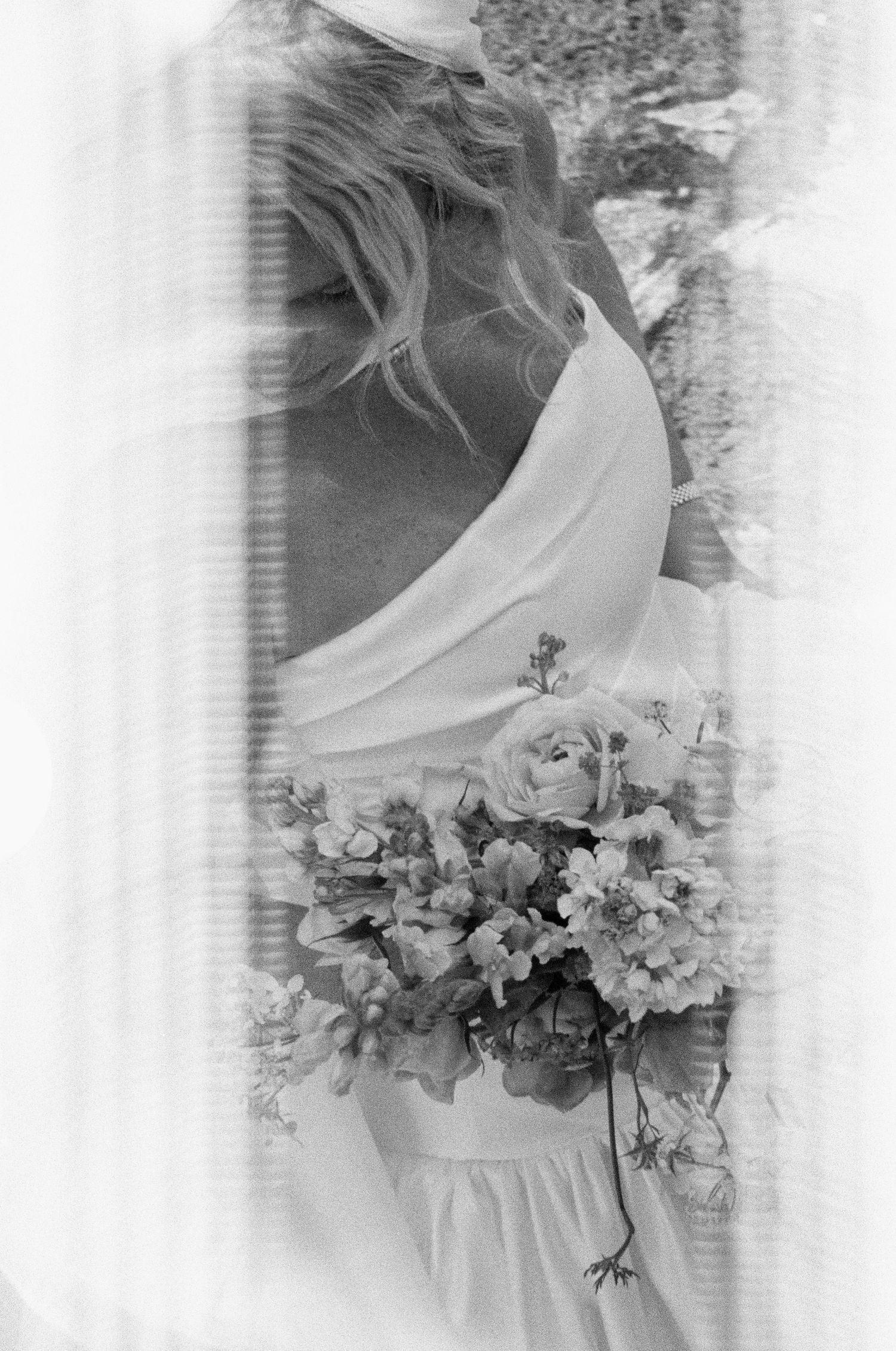 Ethereal black and white photograph of flowing wedding dress with floral bouquet.