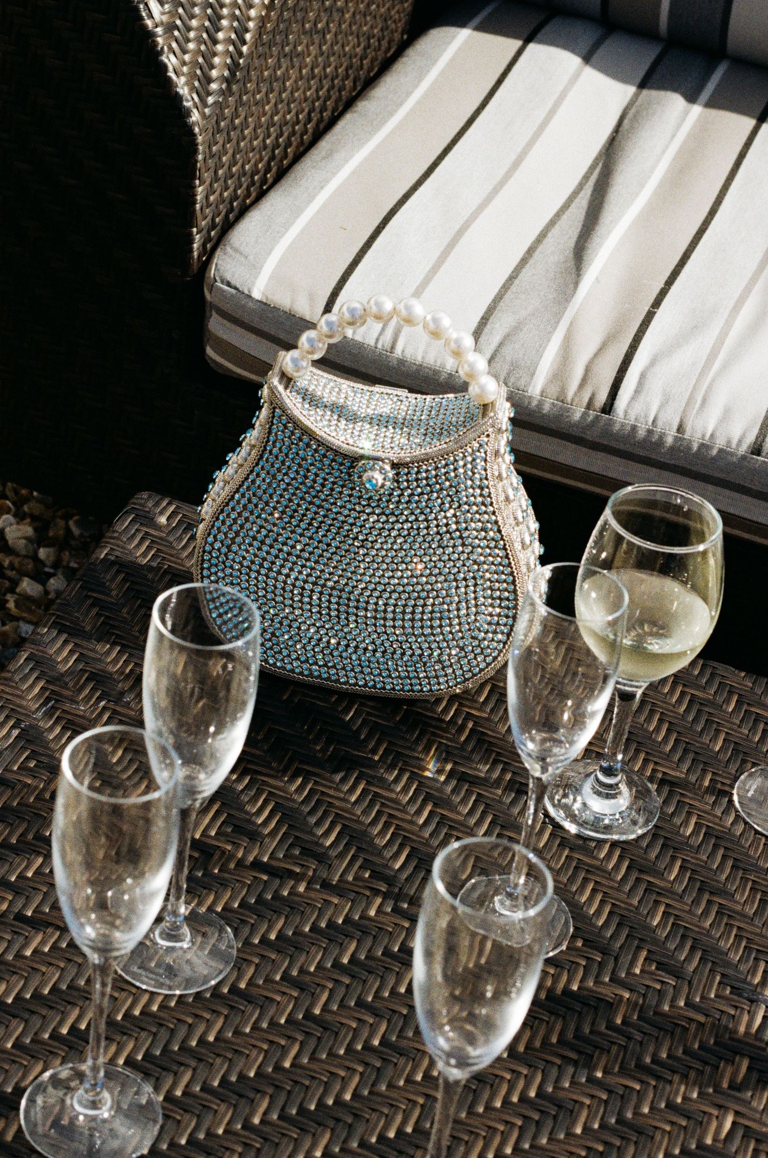 Elegant pearl beaded purse displayed with empty wine glasses on a woven surface.