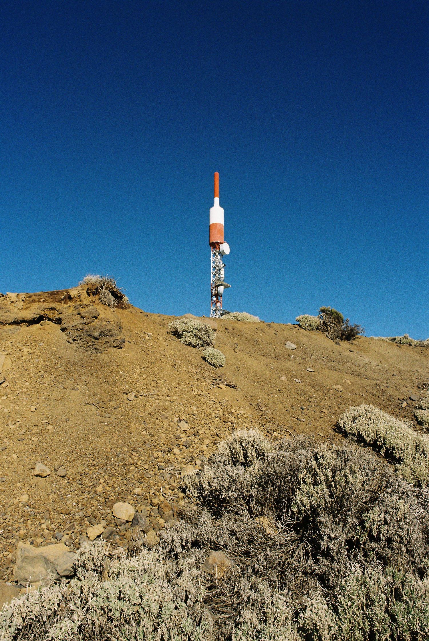 Communications equipment and towers stand atop a barren mountain ridge against deep blue sky.