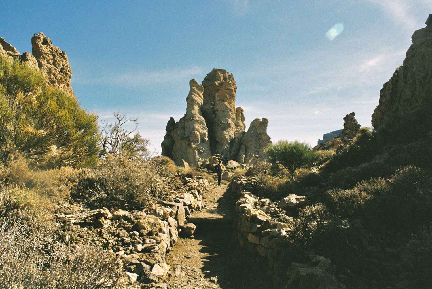 Rocky desert canyon formations under bright blue skies with dramatic shadows.