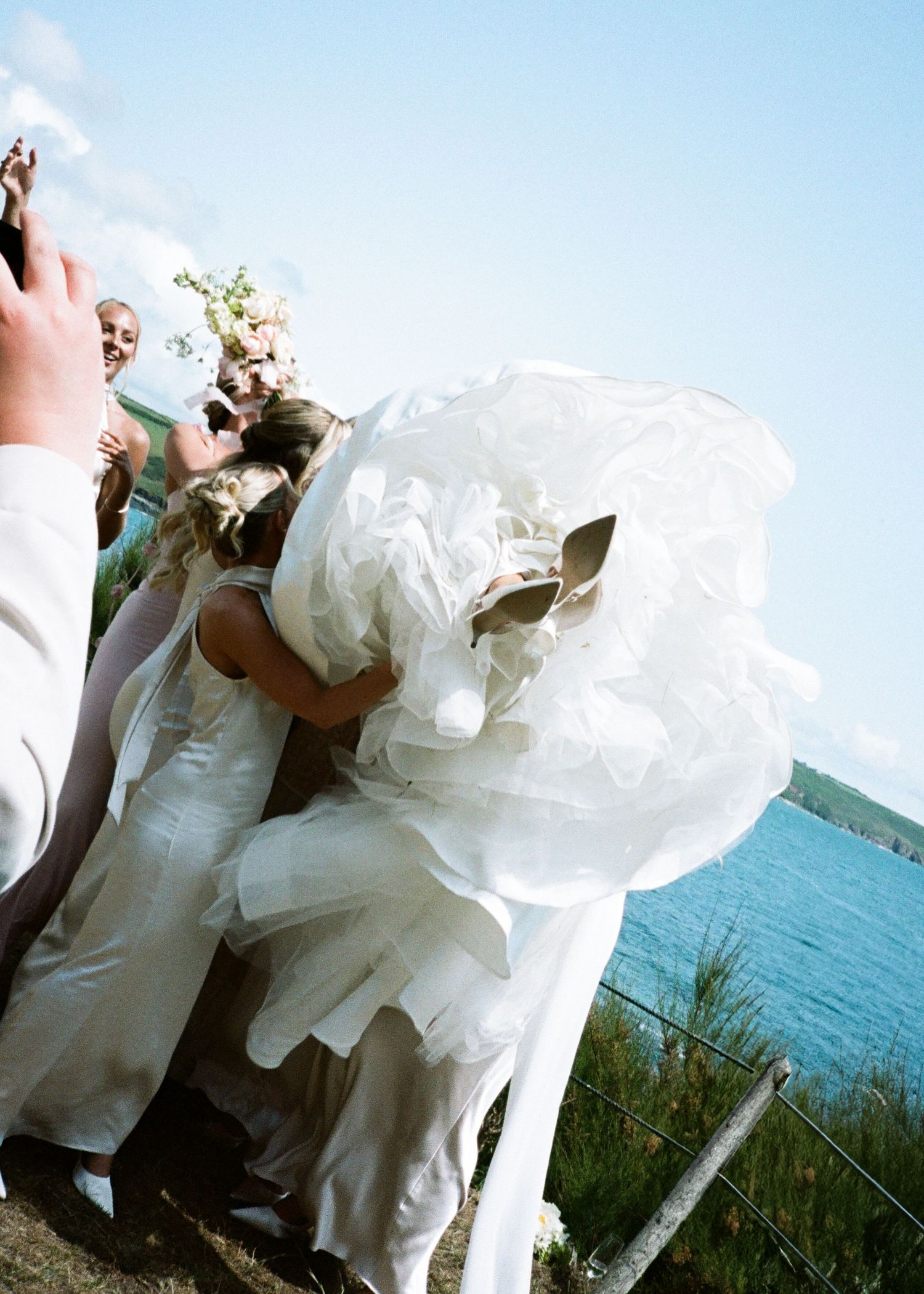 Wedding couple in white attire photographed against blue ocean backdrop.