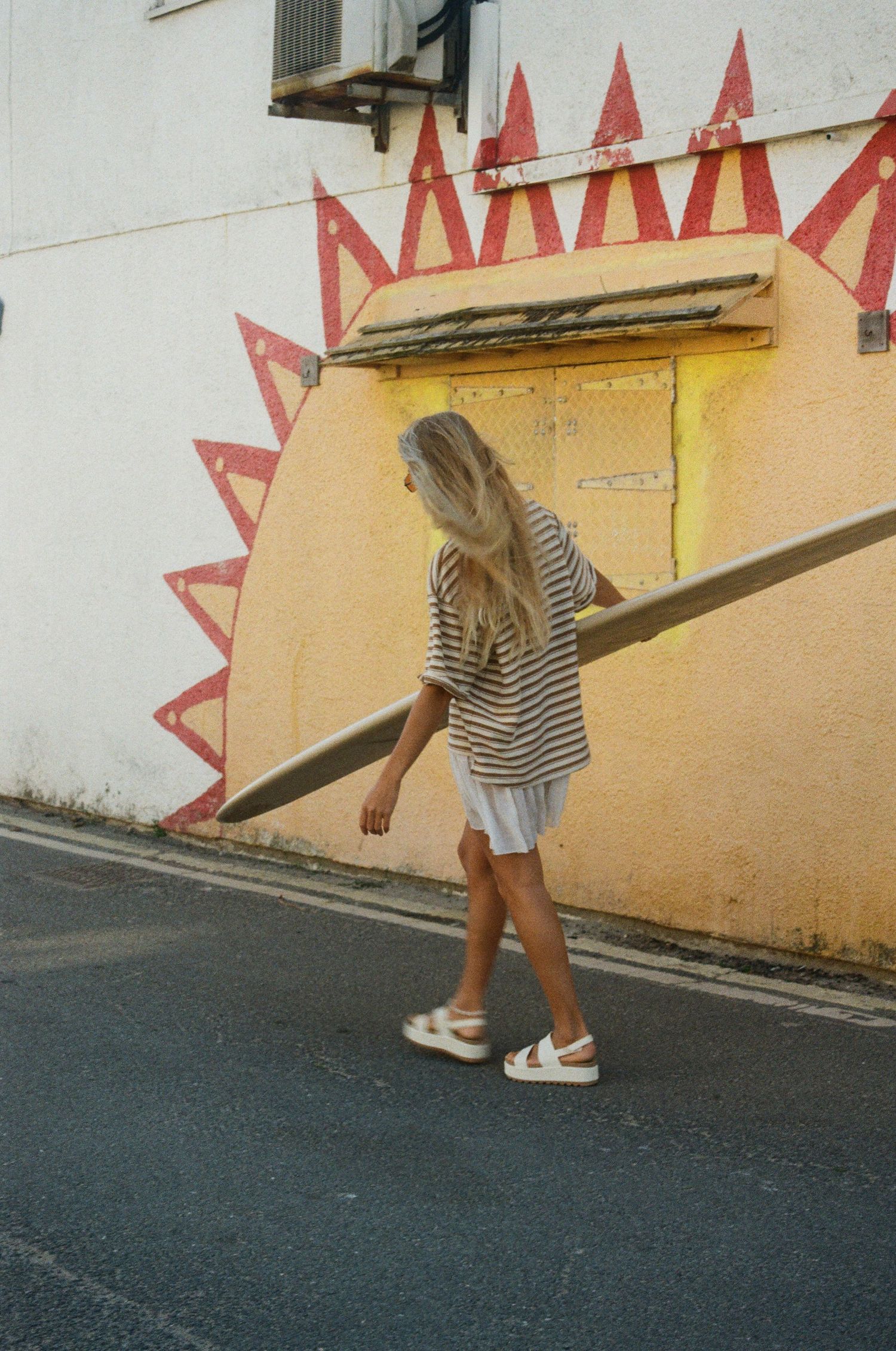 Person in striped shirt walking down a yellow-walled alley with geometric red designs.