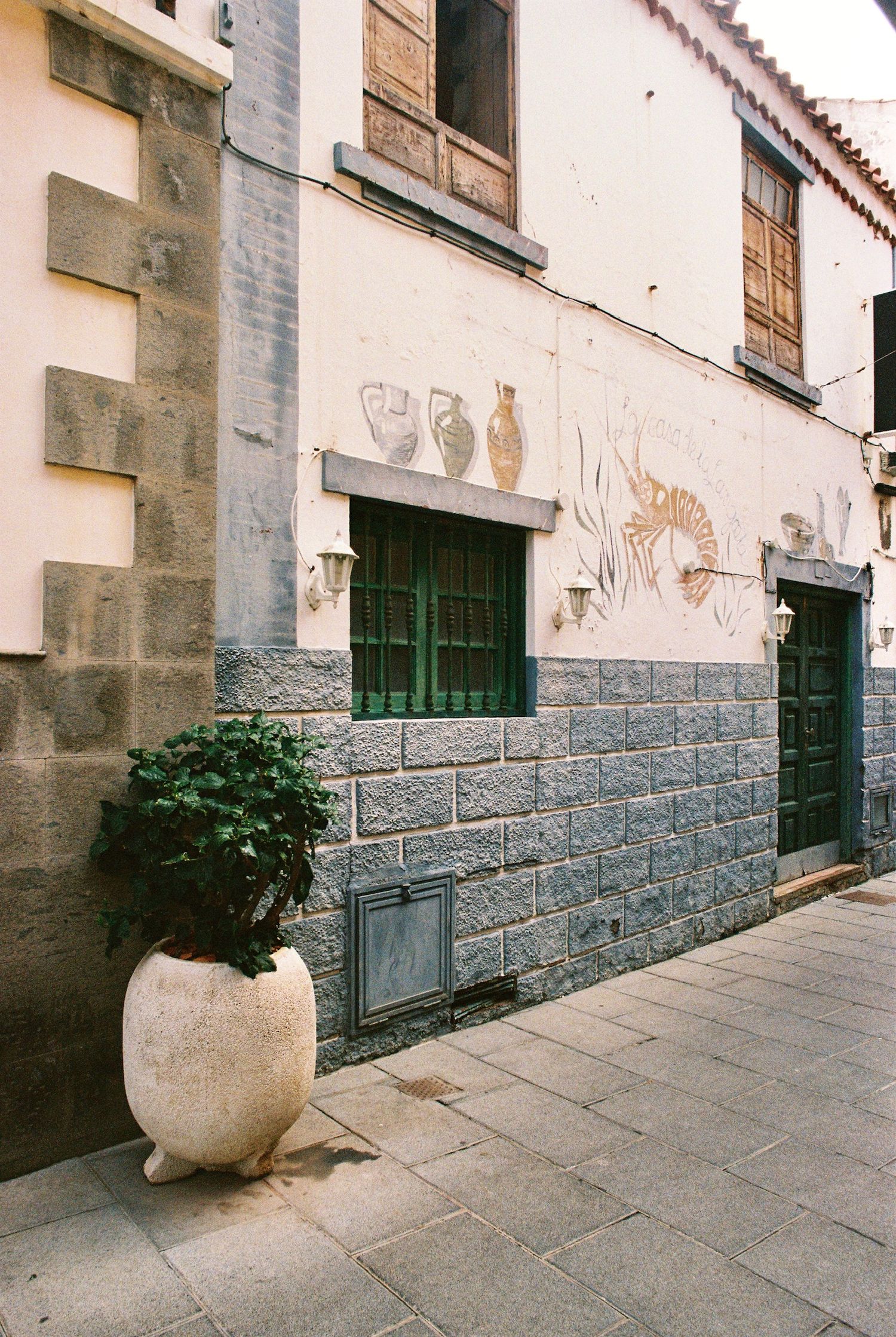 White building facade with stone base and green doors along urban sidewalk.