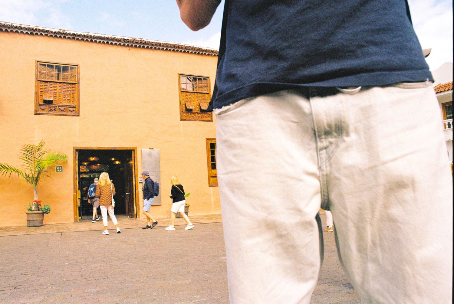 View of people entering a yellow Spanish colonial style building with palm trees.