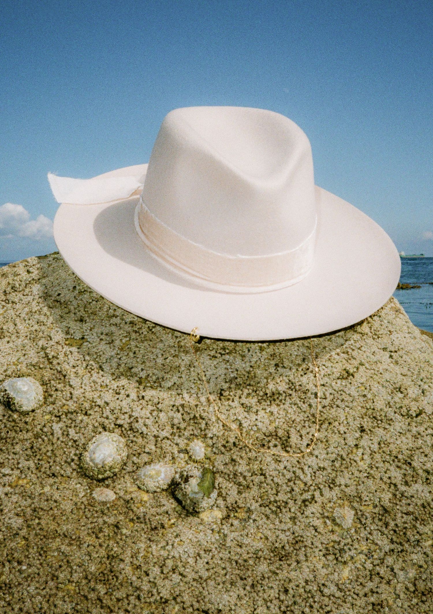 White wide-brimmed hat photographed on rocky coastal terrain against blue ocean backdrop.