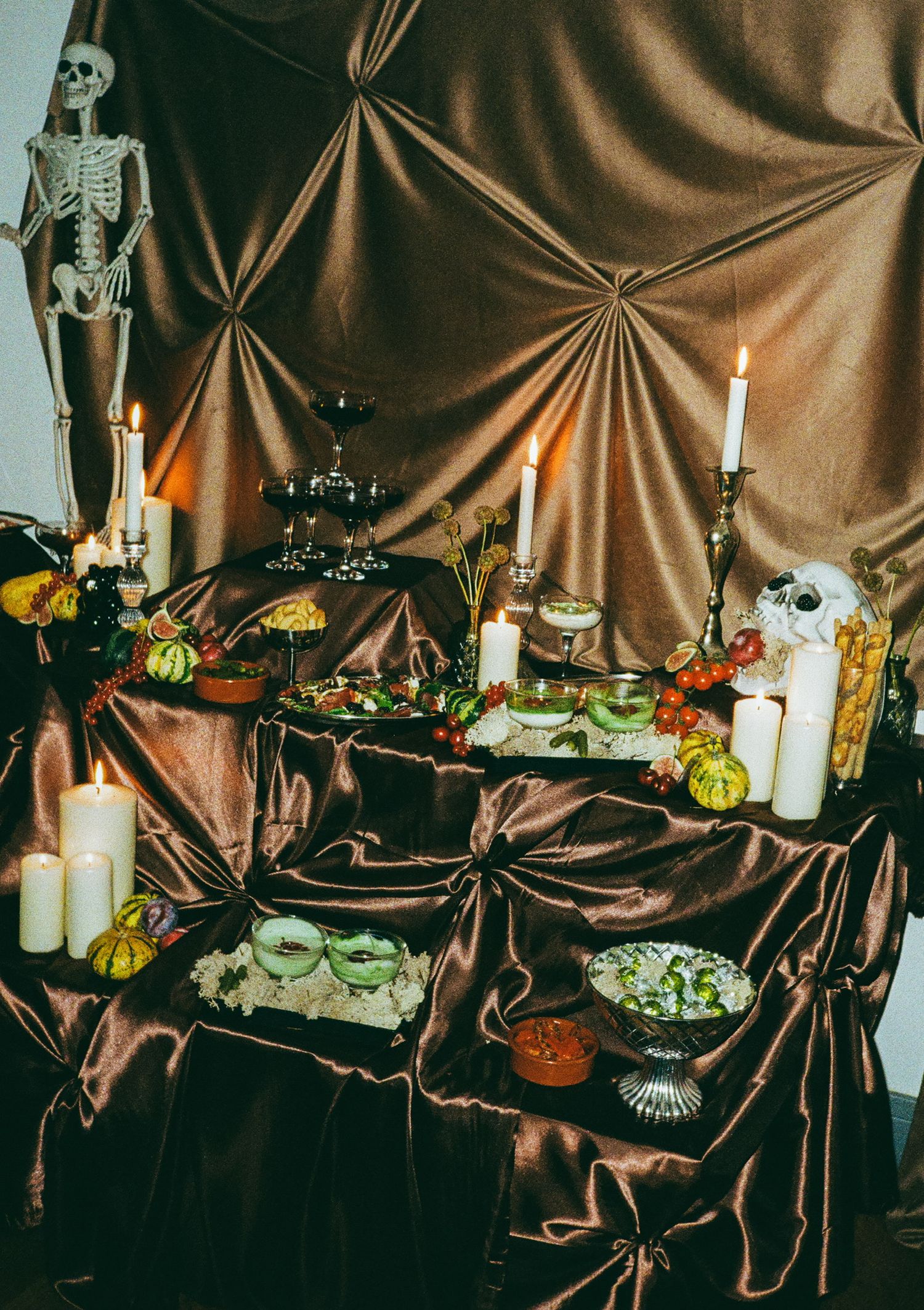 Spooky Halloween party table with skeletons, candles and draped brown fabric backdrop.