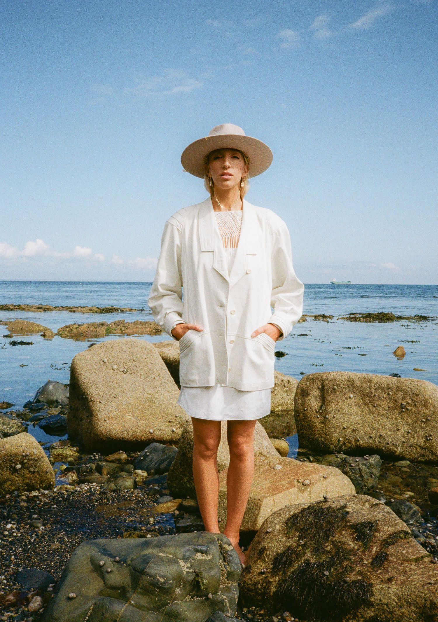 Fashion photography series showing white summer outfit and wide brim hat at rocky beach location.