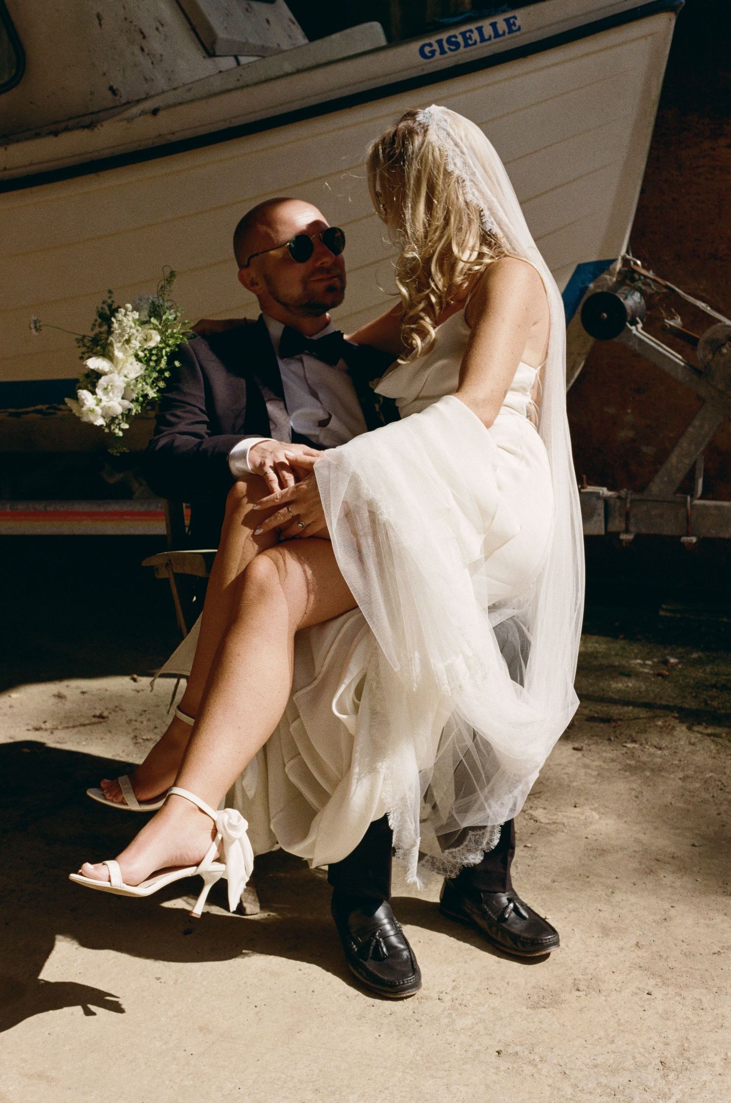 Wedding couple's feet shown sitting together, bride in white heels and groom in formal shoes.