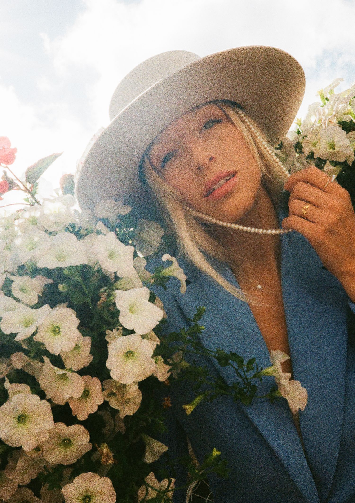Dreamy portraits with white flowers showing someone in a beige hat and blue blazer.