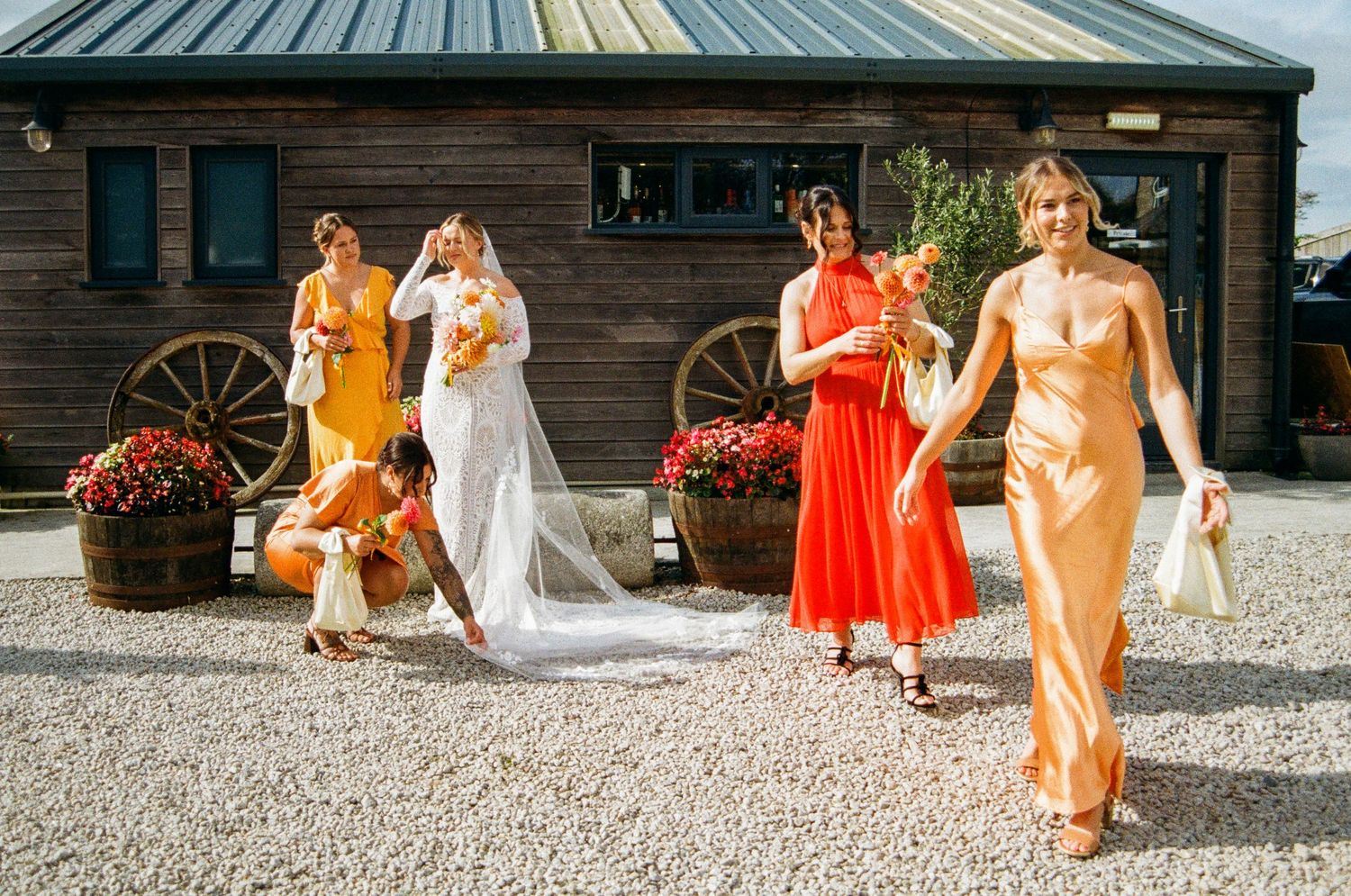 Wedding party members in orange and white attire gathered outside a rustic venue.