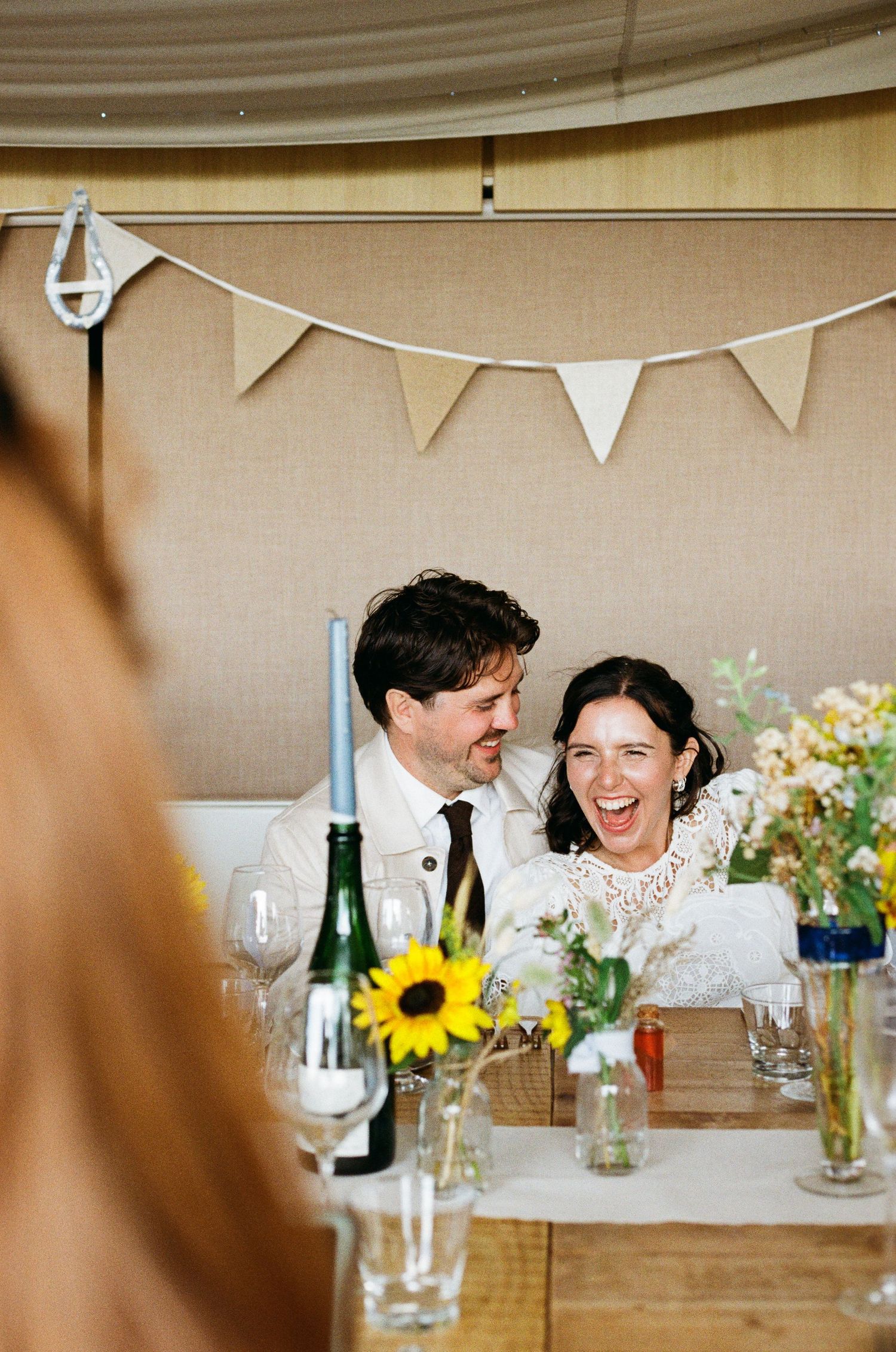 Wedding reception table decorated with sunflowers and bunting under a tent.