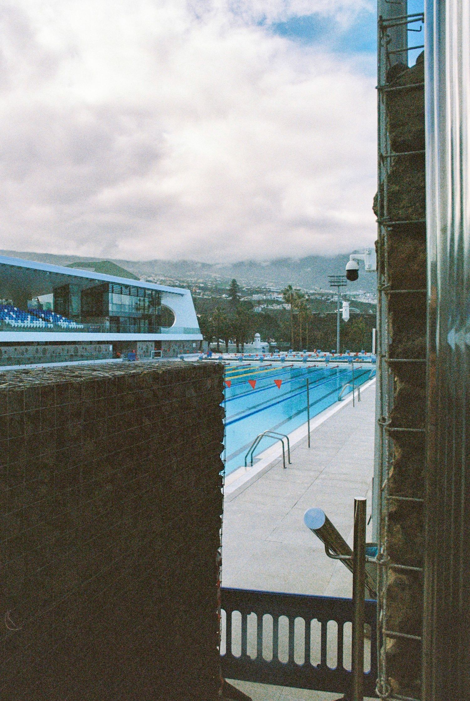 View of an outdoor swimming pool through a window with mountains visible in the distance.