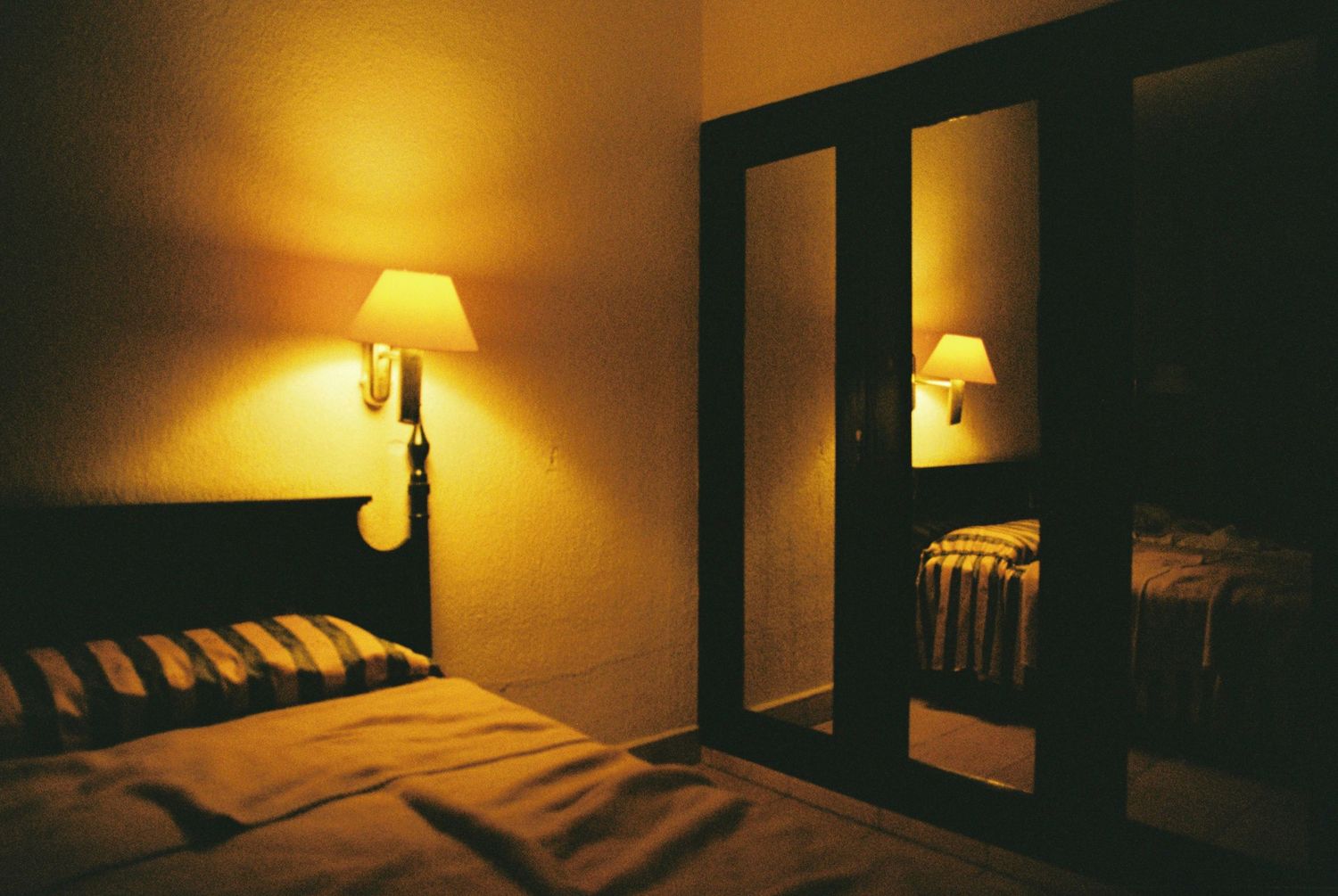 Moody hotel room interior with warm lamp lighting and mirrored closet doors.