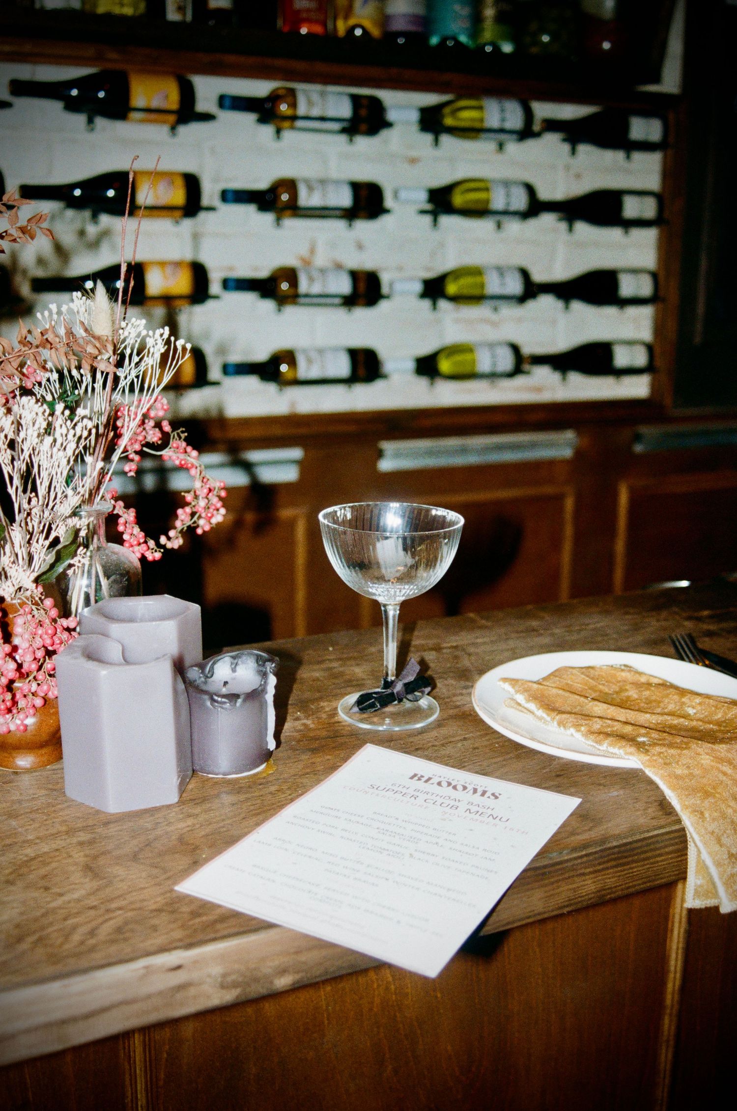 Wine bottles displayed on wall with table setting and menu in foreground.